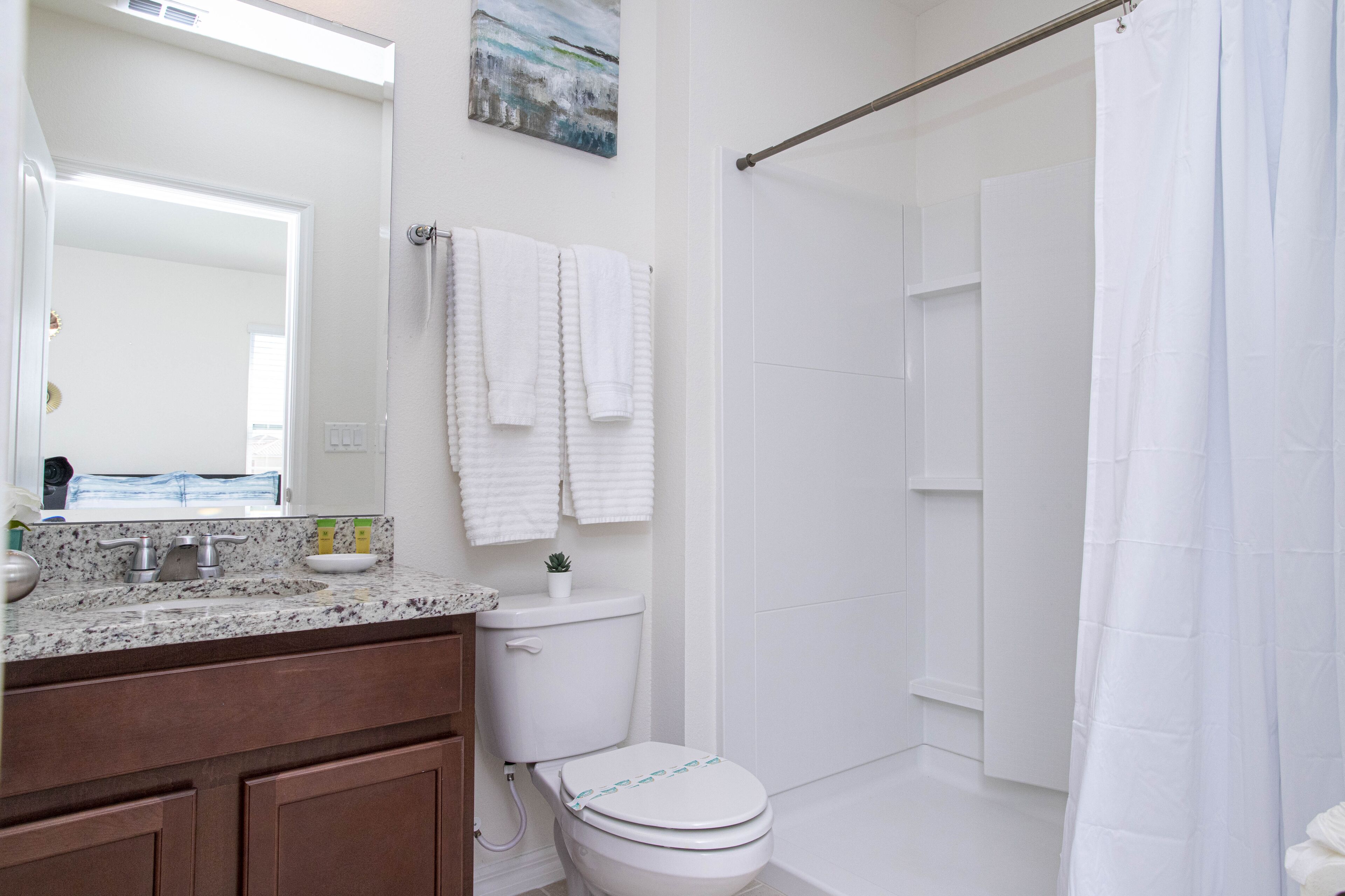 A bathroom with a white toilet, a sink with a marble countertop, and a shower area with a white curtain.