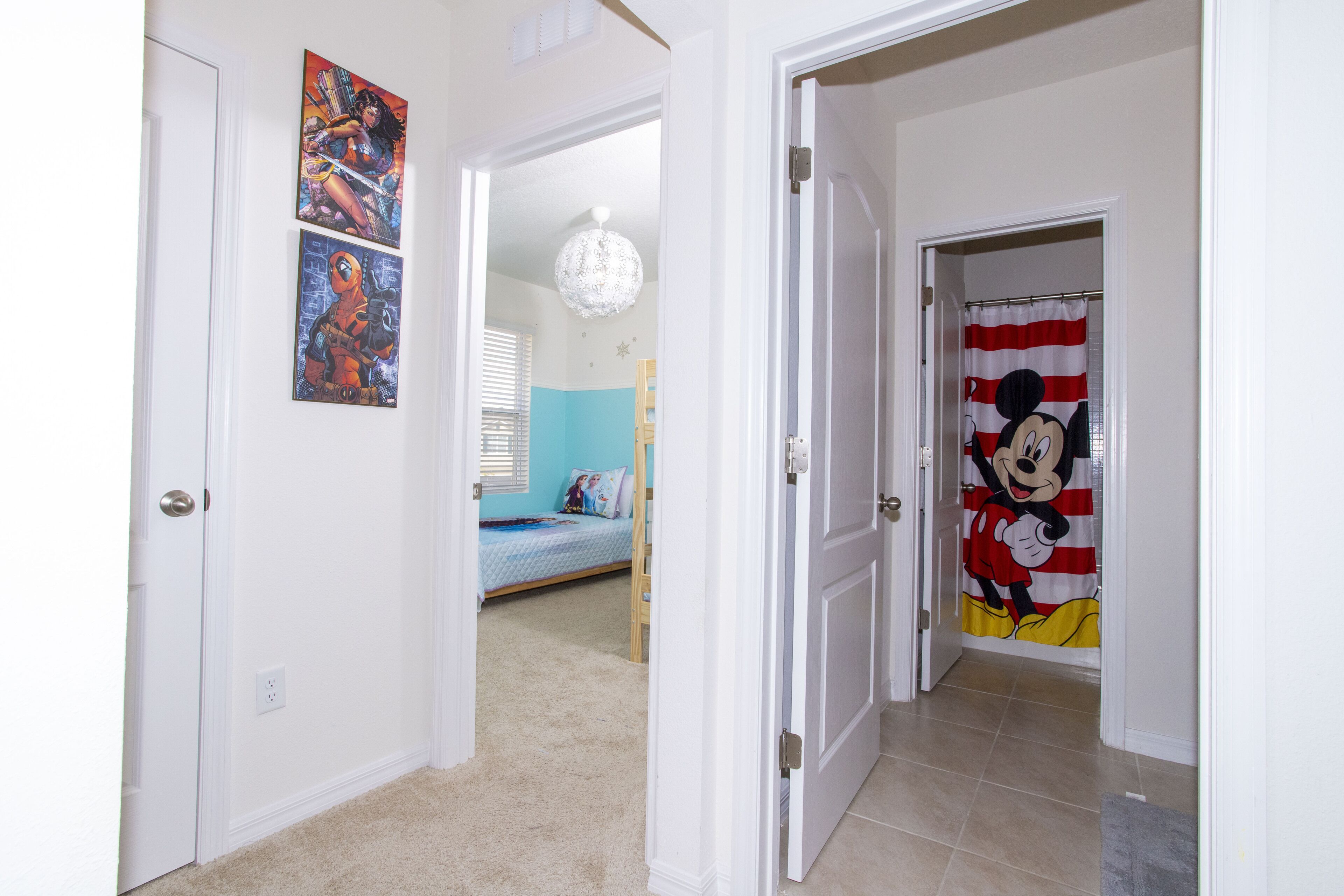 A hallway with a bed, a Mickey Mouse curtain, and a door leading to another room.