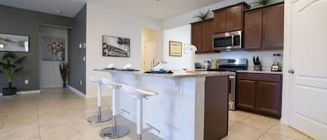 Una cocina moderna con una isla central, taburetes de bar, microondas y lavavajillas.