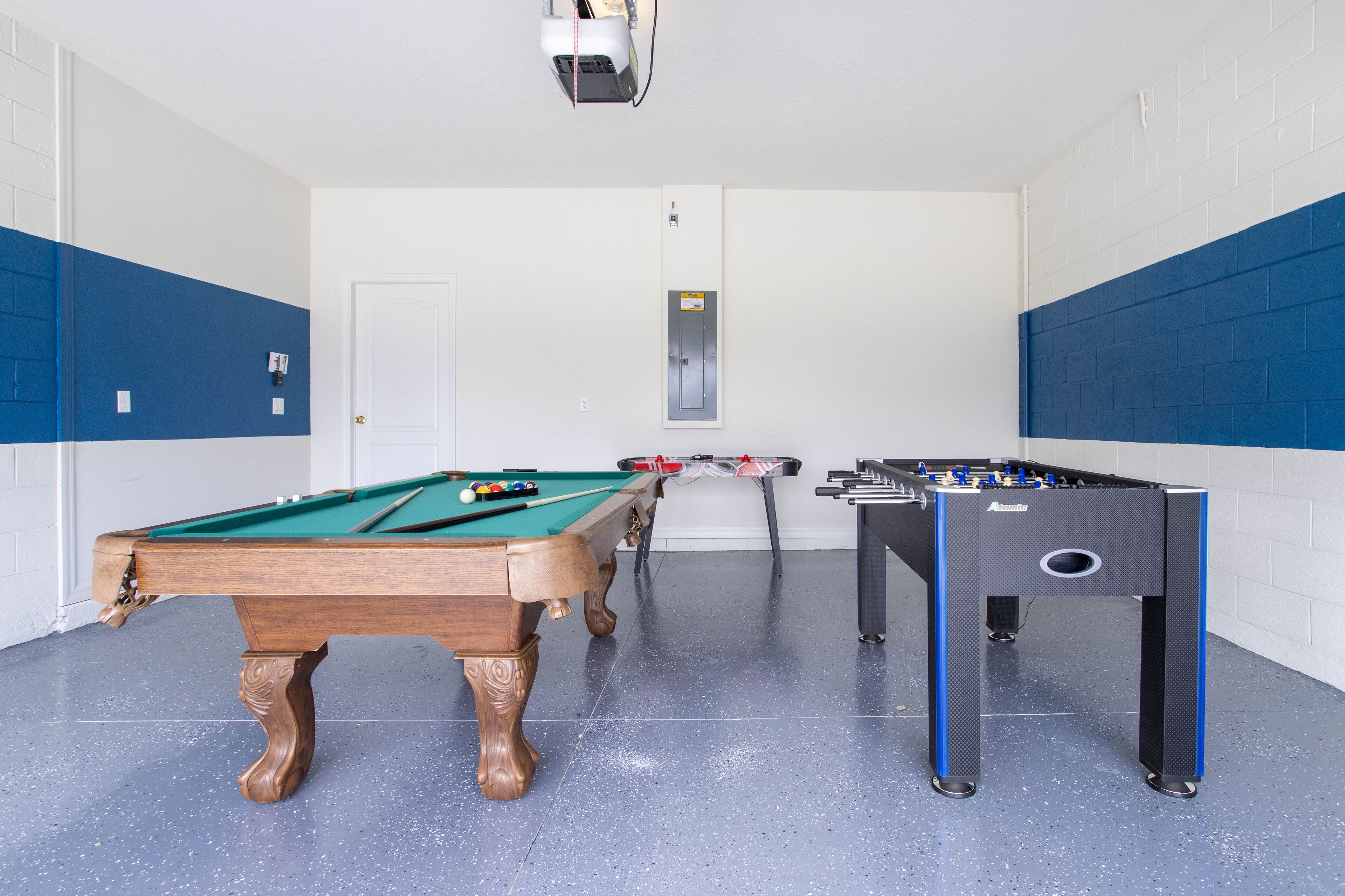 Een pooltafel, een tafelvoetbaltafel en een deur in een kamer met blauwe en witte wanden.