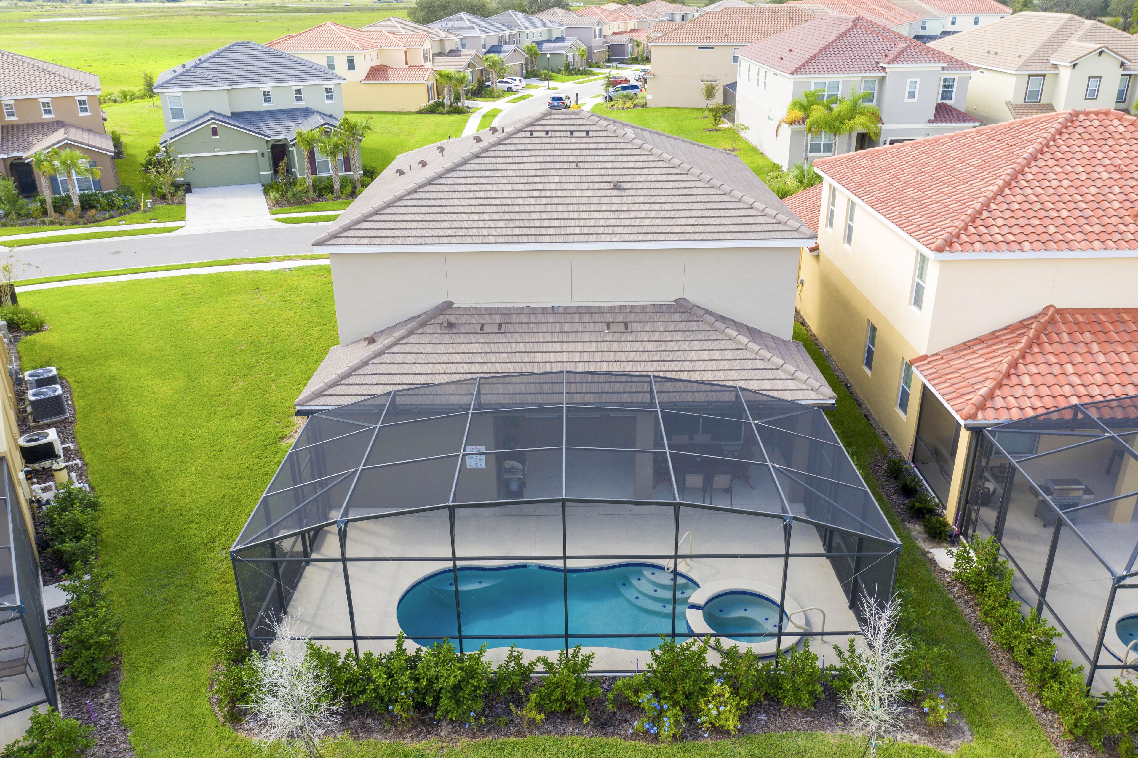 Zona residencial con una amplia piscina rodeada por una terraza cubierta, casas al fondo y un césped bien cuidado.