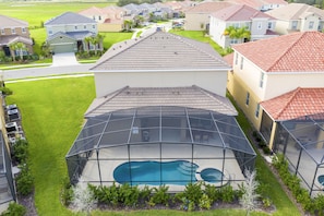 Uma área residencial com uma grande piscina cercada por um deque coberto, casas ao fundo e um gramado bem cuidado.