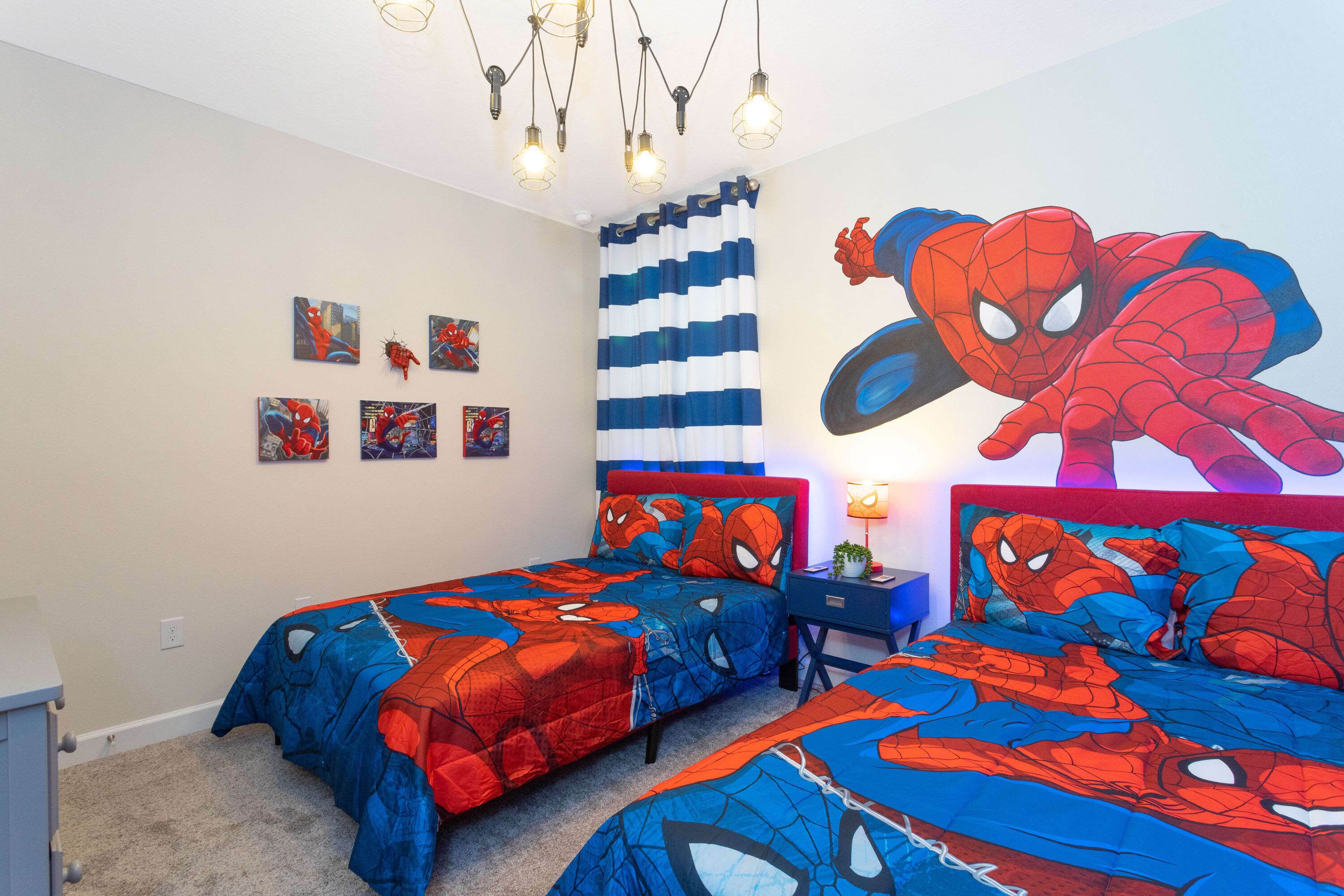A bedroom with two beds, each covered in Spider-Man themed bedding. There are wall art pieces and a Spider-Man mural.