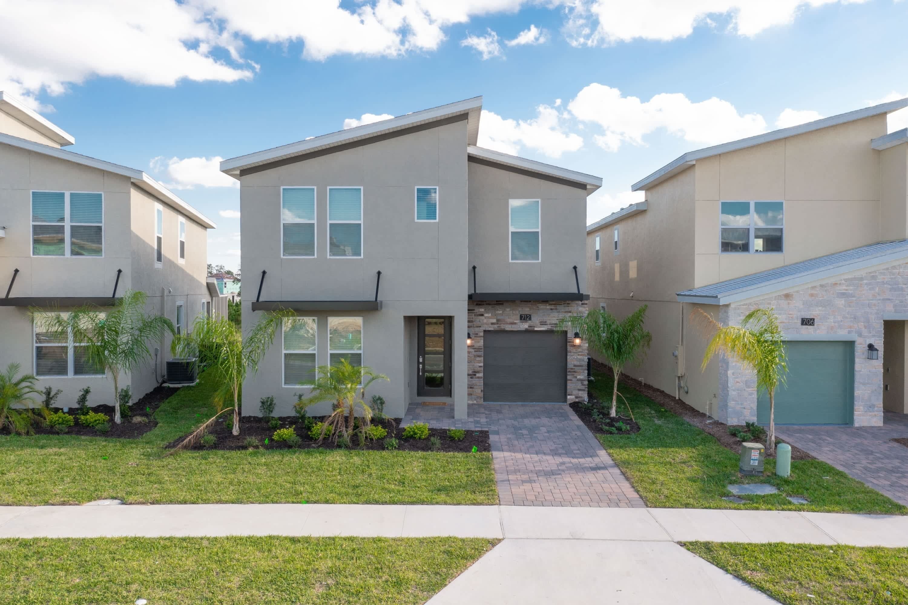 A modern two-story residential building with a garage, a landscaped front yard, and a clear sky.