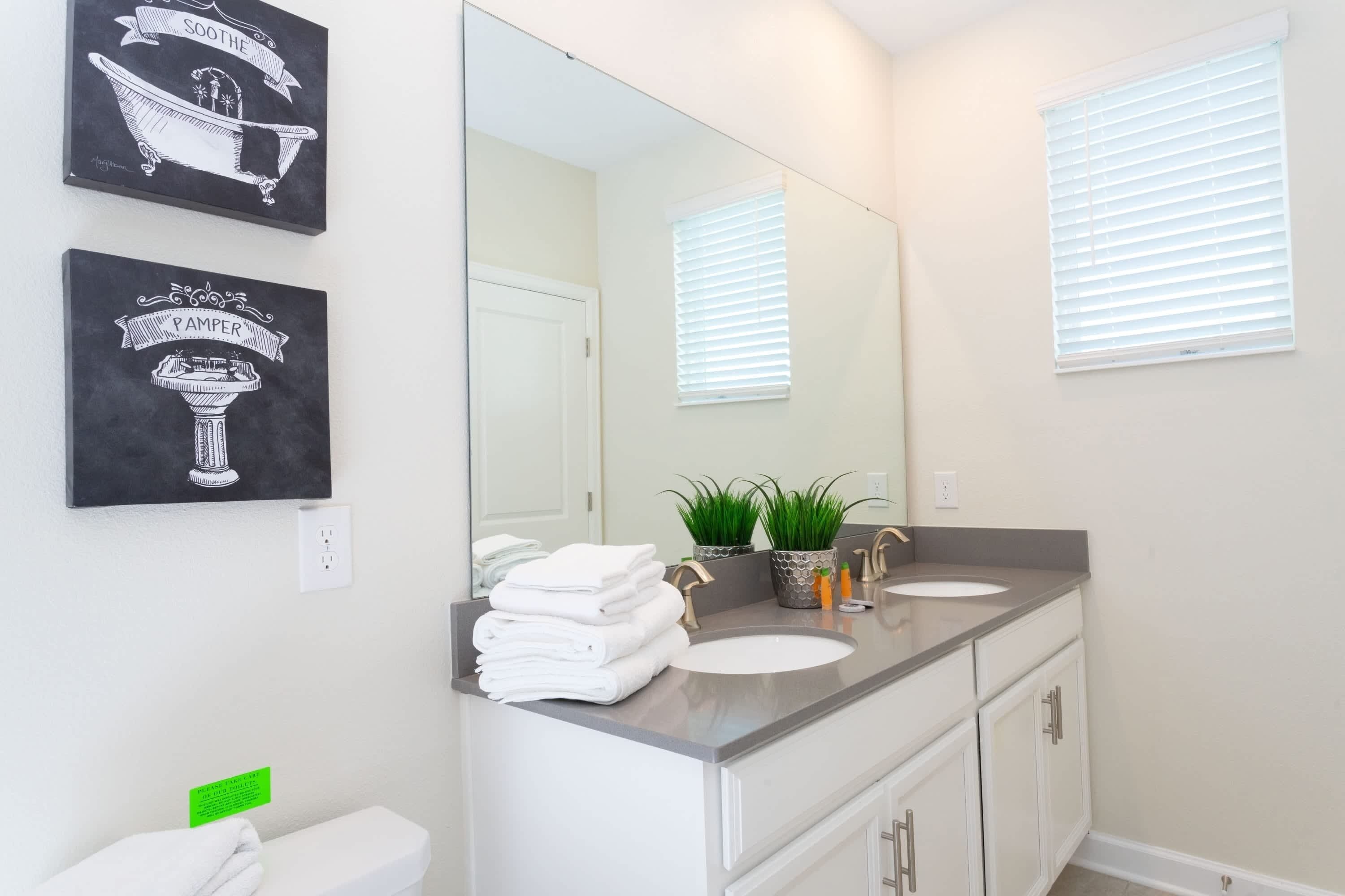 A modern bathroom with a large mirror, two sinks, a toilet, and decorative wall art.