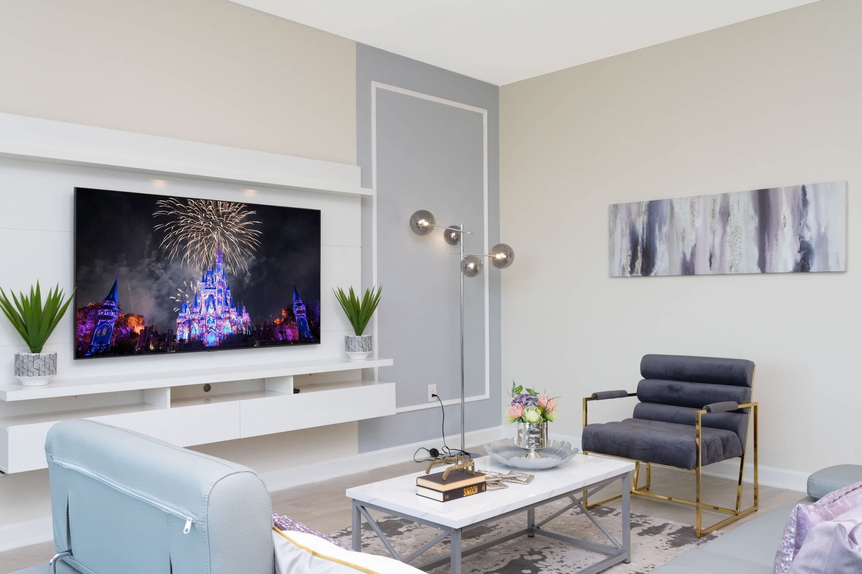 A modern living room with a flat-screen TV, a grey sofa, a coffee table with books and a vase, and a decorative chair.