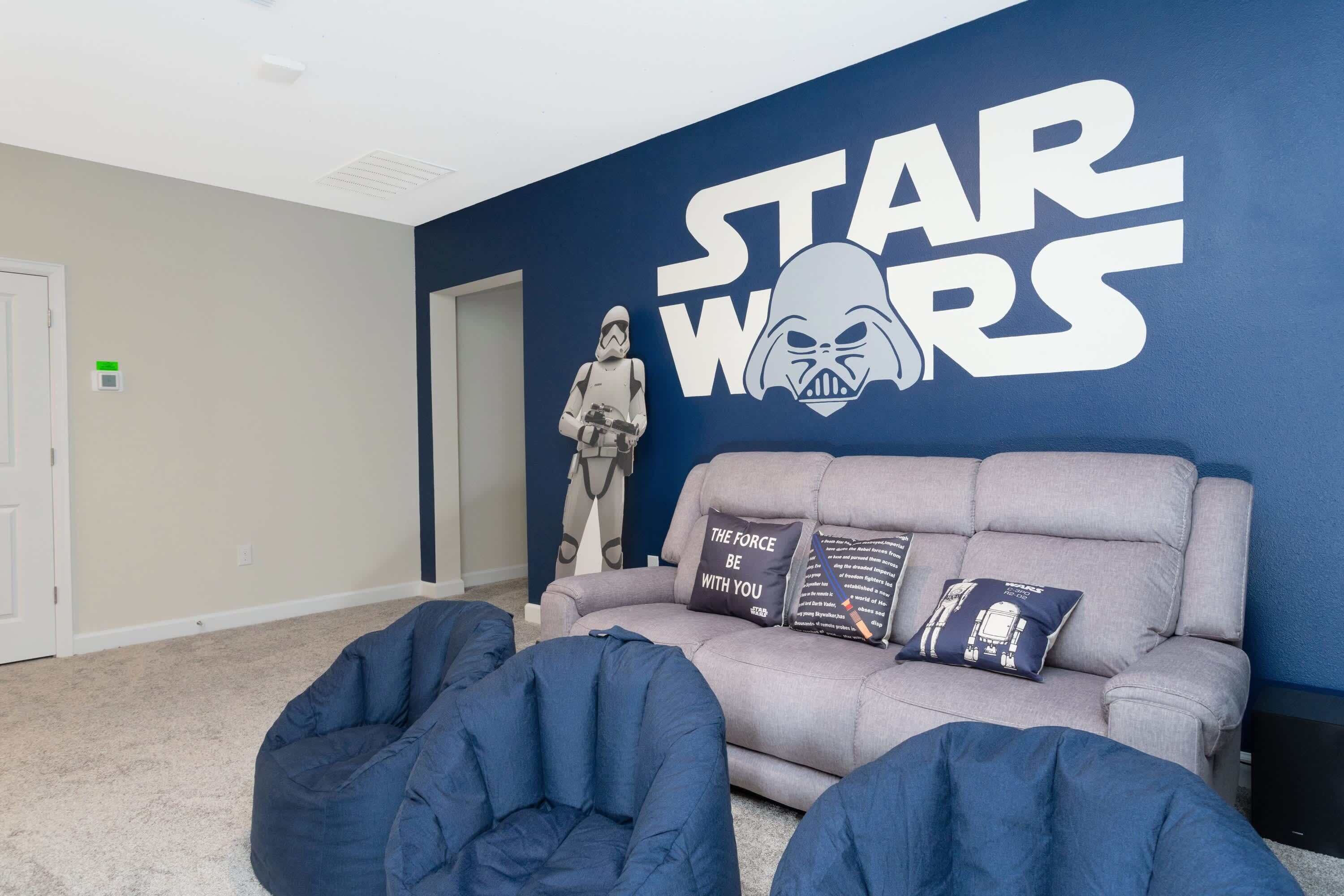 Una habitación con una pared temática de Star Wars, un sofá gris con cojines y dos sillones de peluche.