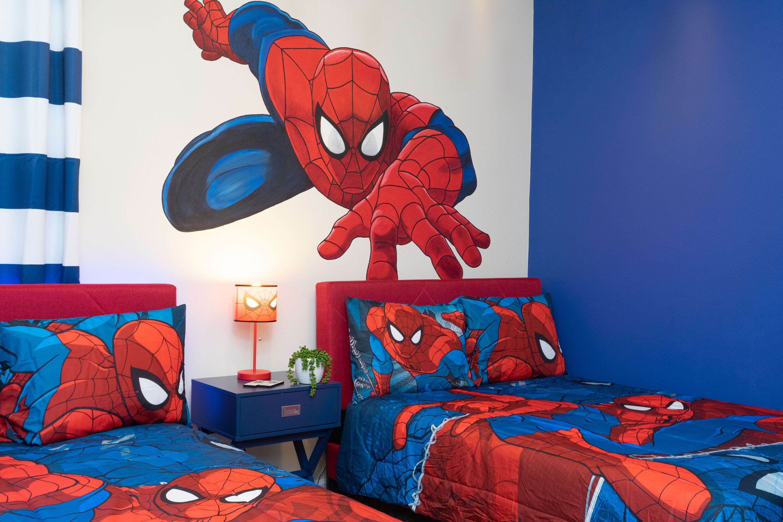 Ein Schlafzimmer mit zwei Betten, beide mit einem Spider-Man Bezug. An der Wand befindet sich ein Wandbild von Spider-Man in einer dynamischen Pose.