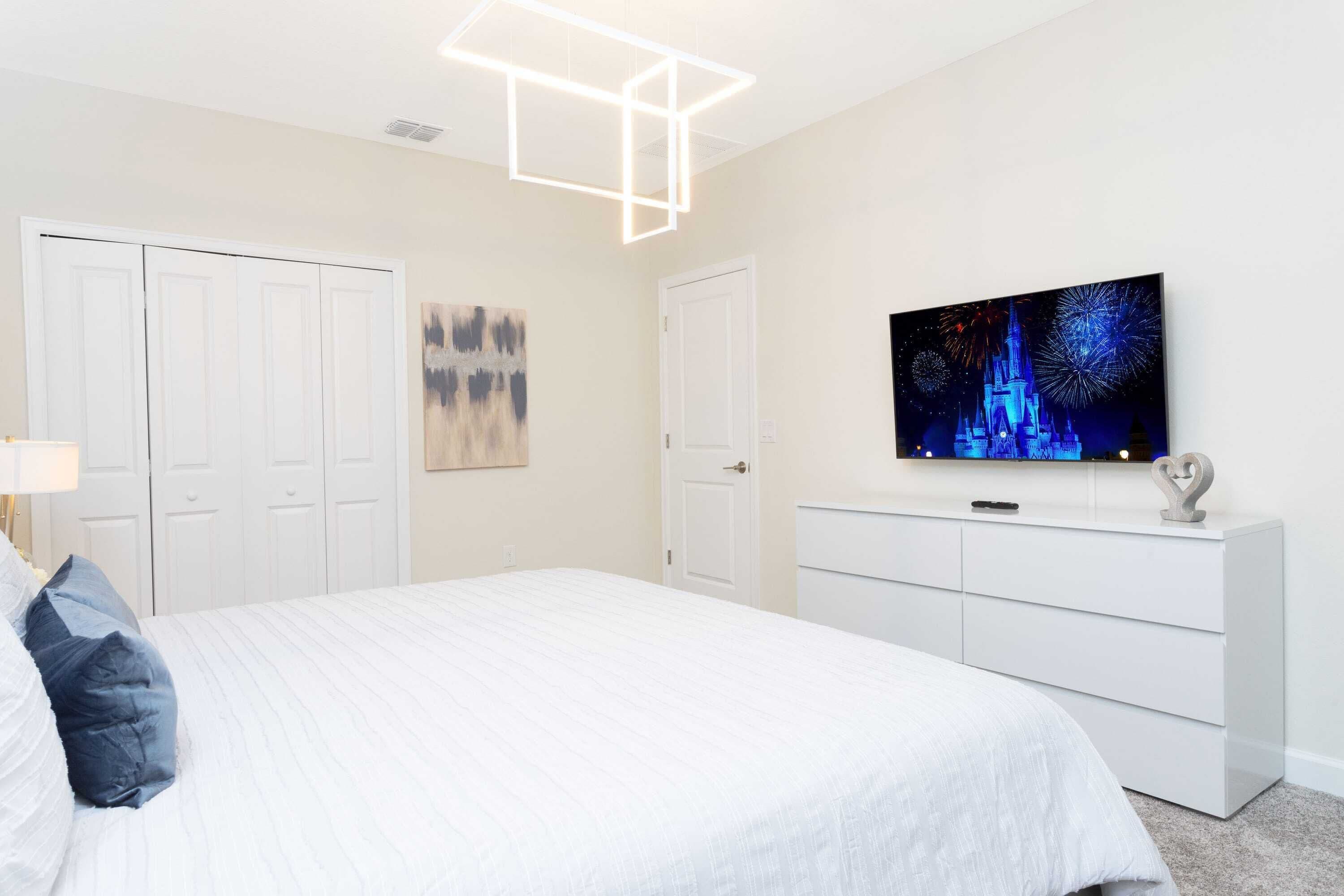 Un dormitorio con cama, cómoda, televisor en la pared y puerta.