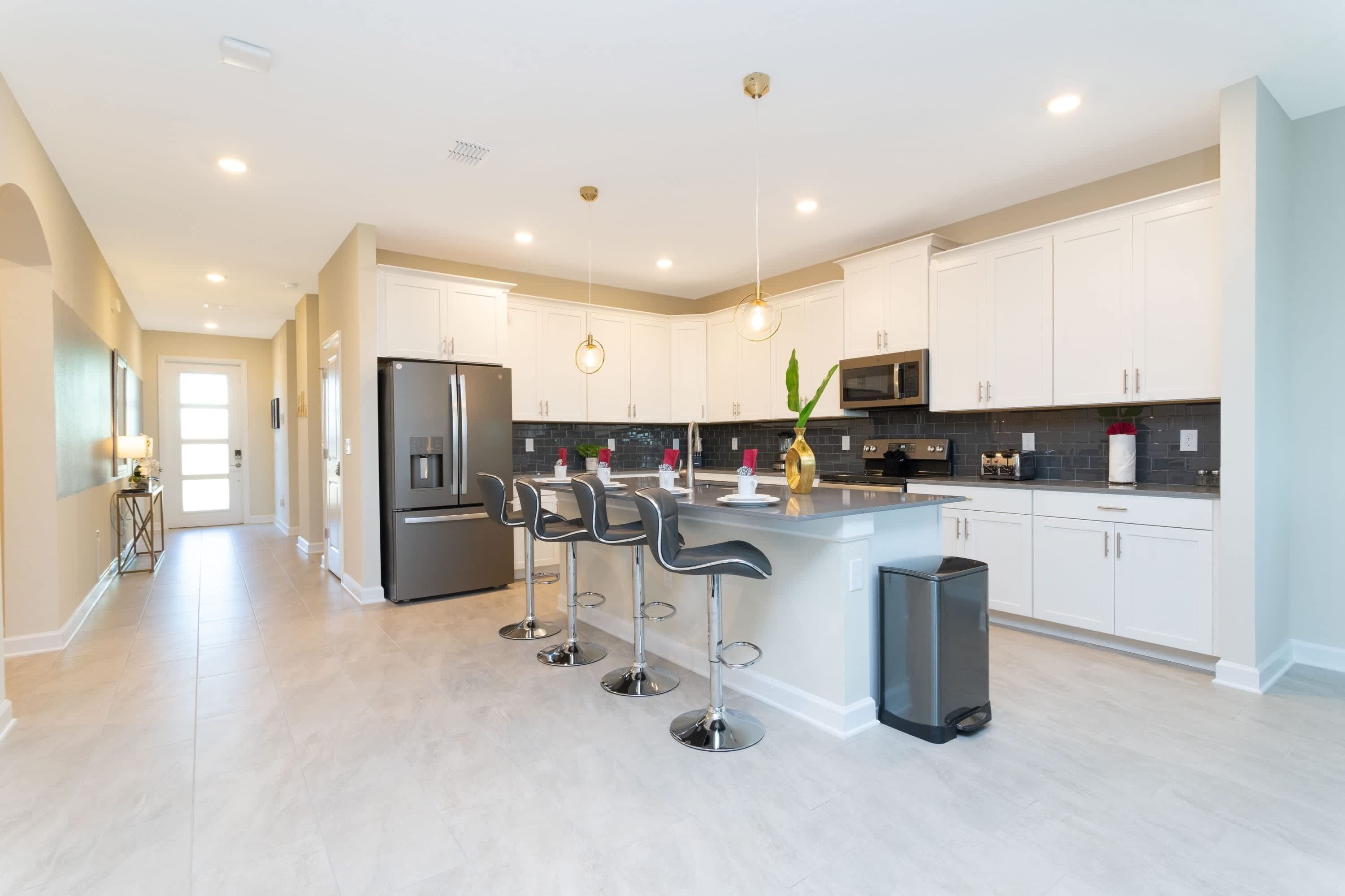 Una cocina moderna con armarios blancos, electrodomésticos de acero inoxidable y una isla central con taburetes de bar.