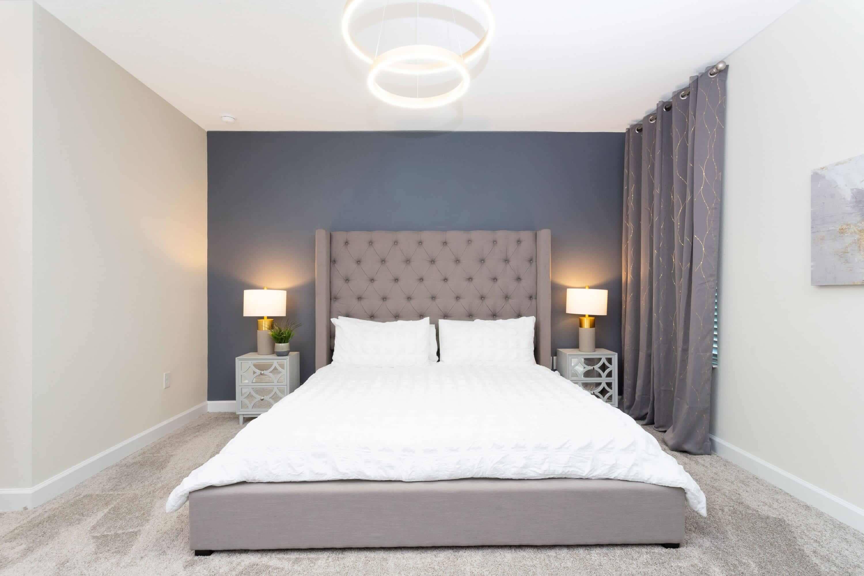 Een slaapkamer met een groot bed, twee nachtkastjes met lampen, een gestuufd hoofdeinde en een modern lamparmatuur.