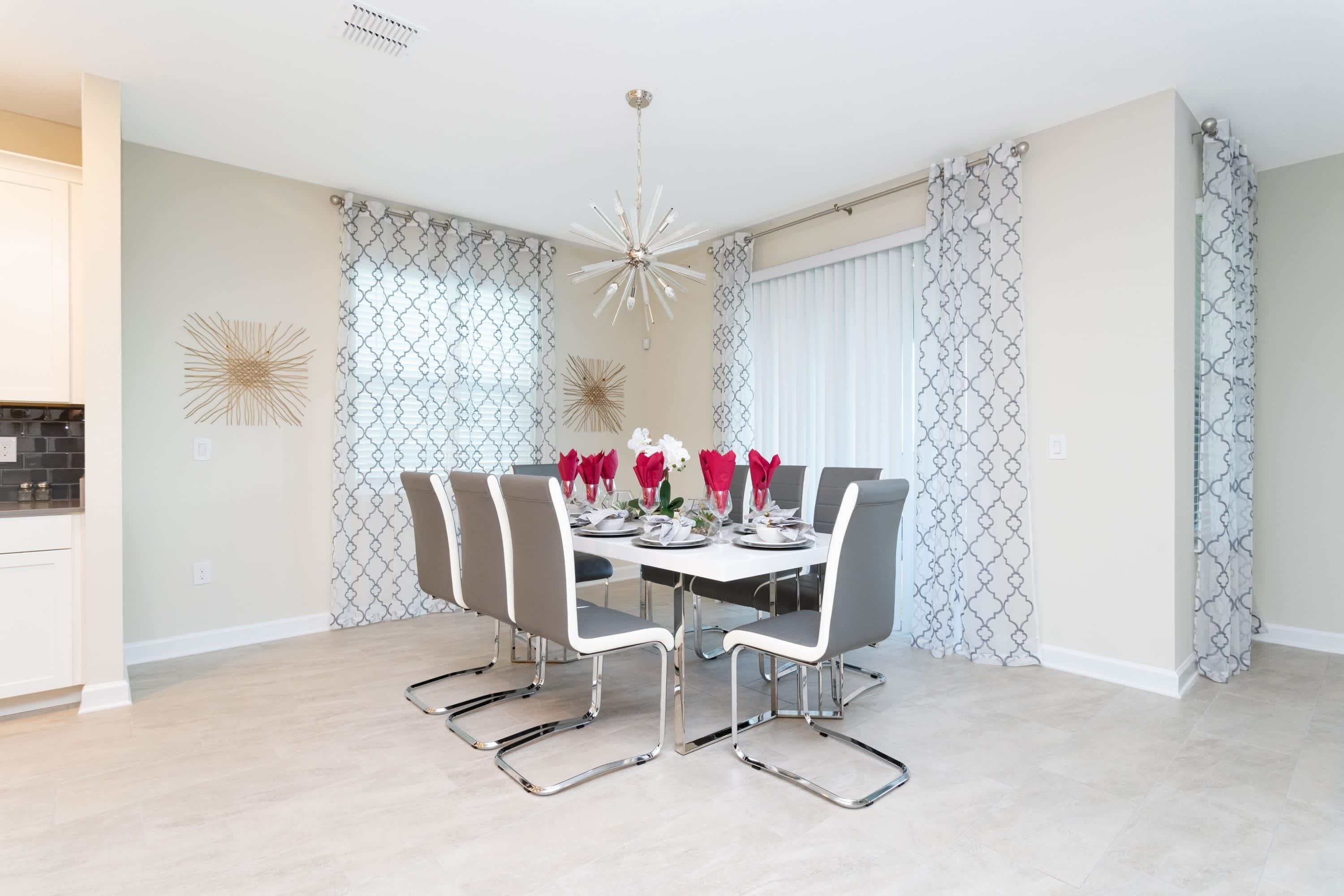 Un comedor con una mesa blanca dispuesta para seis personas, rodeado de sillas grises con patas cromadas.