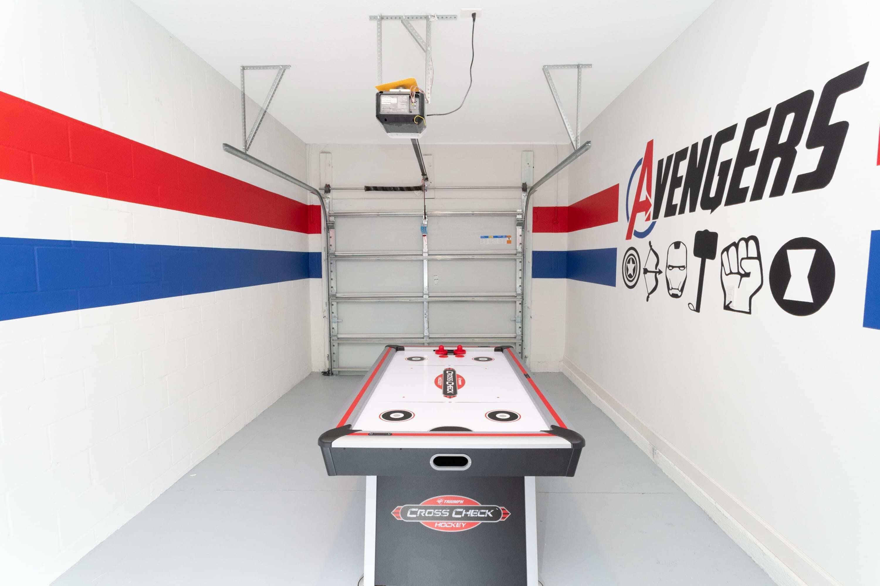 Ein Tischkicker mit dem Schriftzug 'Cross Check', ein an der Decke befestigter Projektor und ein Wandbild mit dem Thema 'Avengers'.