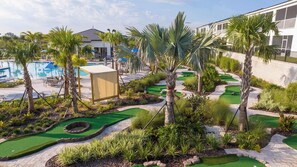 Un campo de golf con piscina, palmeras y un edificio al fondo.
