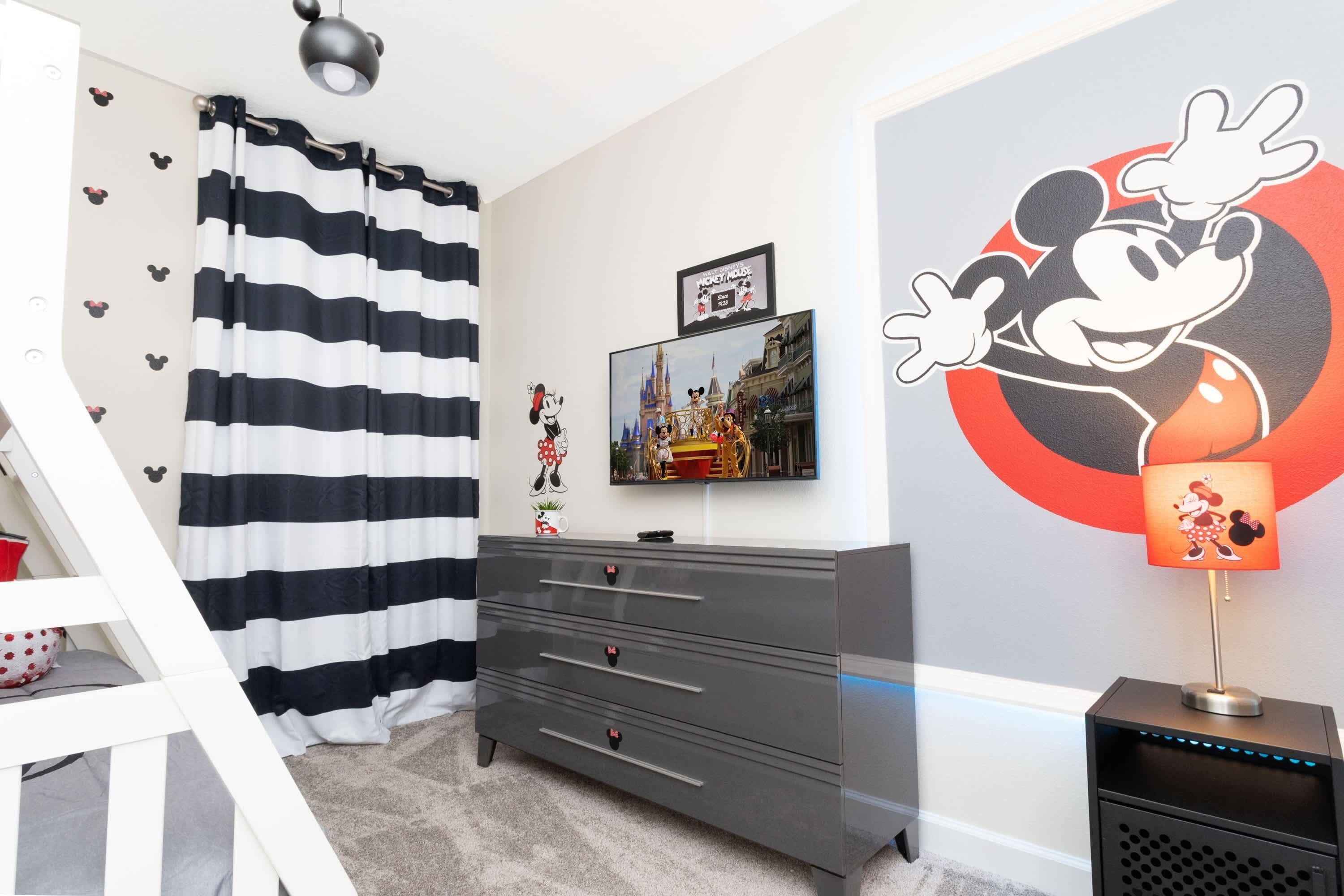 Une pièce avec une commode grise, une fresque représentant Mickey Mouse et un rideau à rayures.