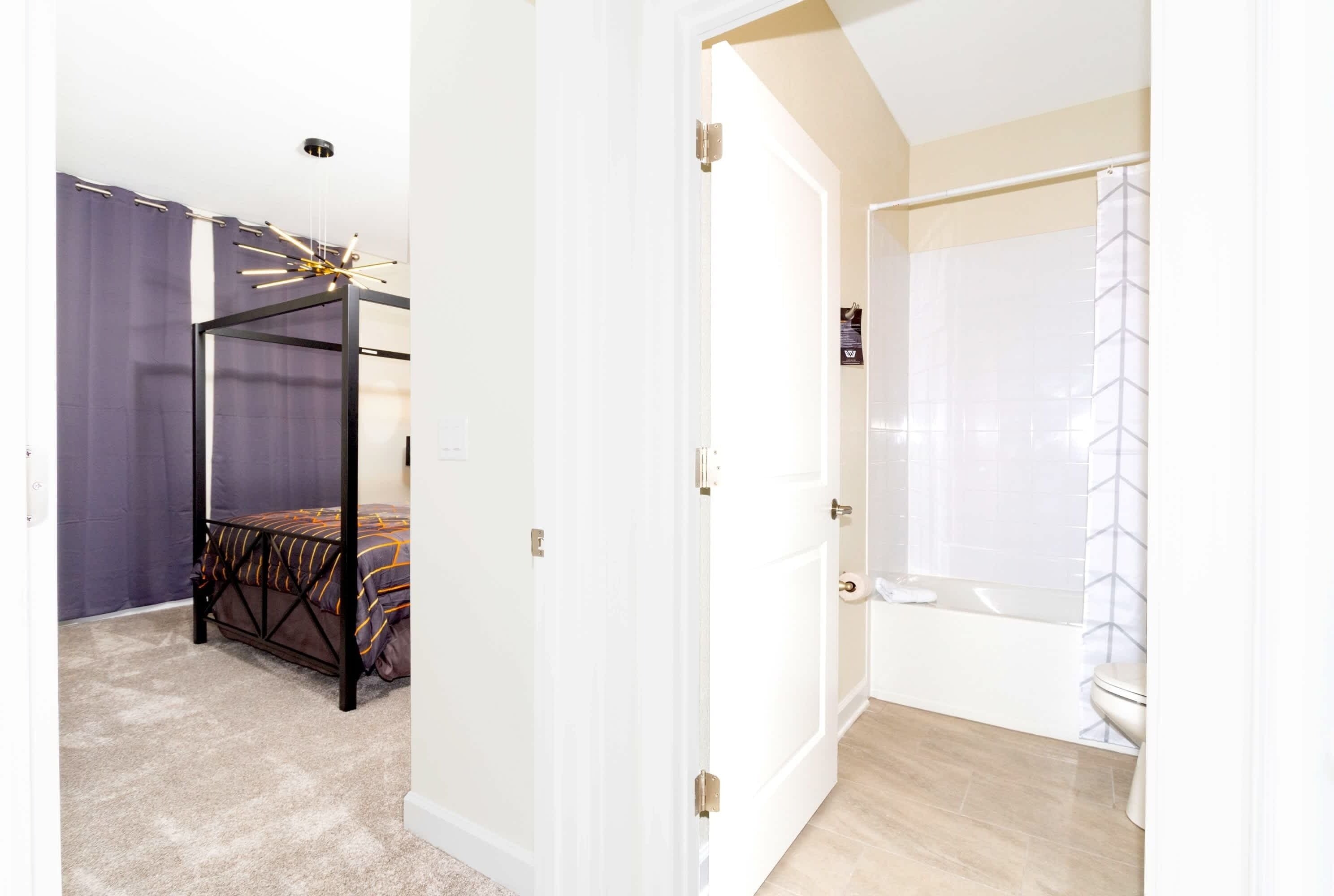 A bedroom with a bed, a bathroom with a bathtub, and a door leading to another room.