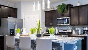 A modern kitchen with dark cabinets, stainless steel appliances, and a blue island with bar stools. - Stunning 5Bd w/ Pool Close to Disney @ Solterra 7829 (Davenport)