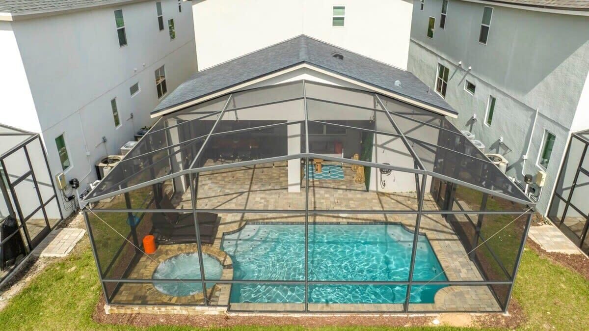 Una piscina cubierta con cerramiento de vidrio, rodeada por un patio de ladrillo y una zona ajardinada.