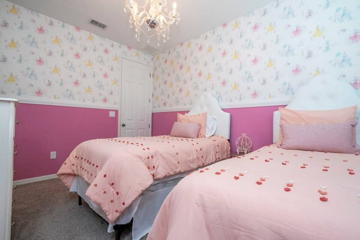 Camera da letto con due letti, biancheria rosa e un lampadario.
