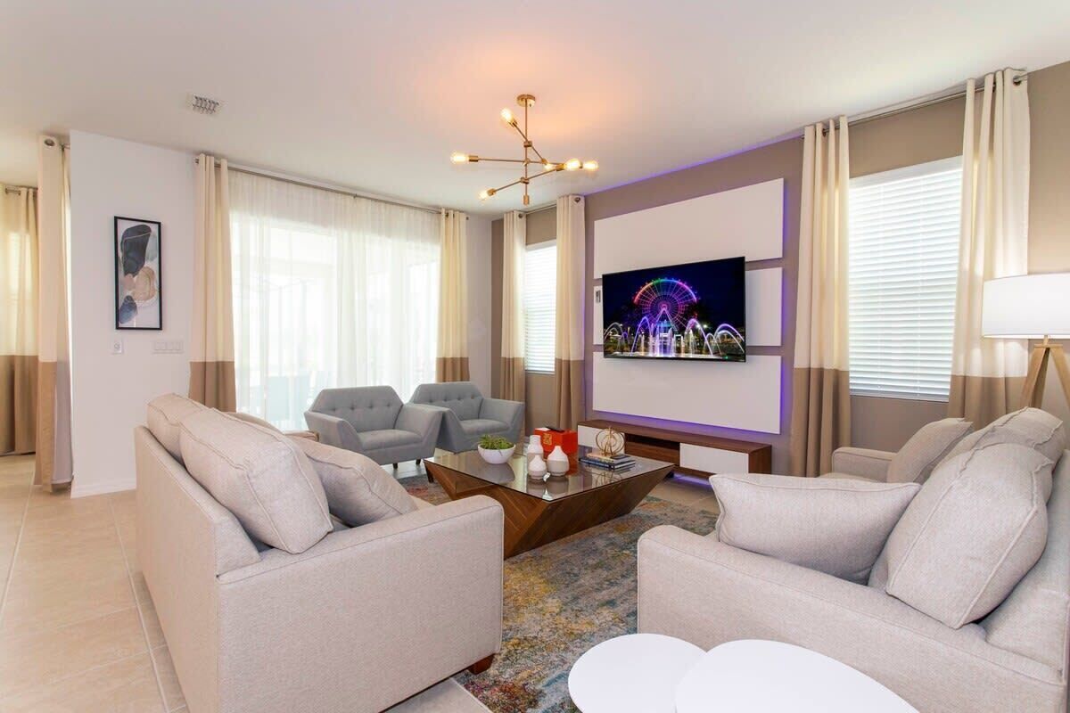 Ein modernes Wohnzimmer mit einem großen Flachbildfernseher, grauen Sofas, einem Couchtisch und einer Deckenleuchte.