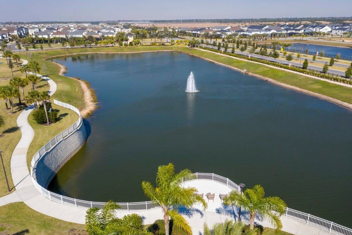 A large pond with a fountain, surrounded by a white fence and palm trees.