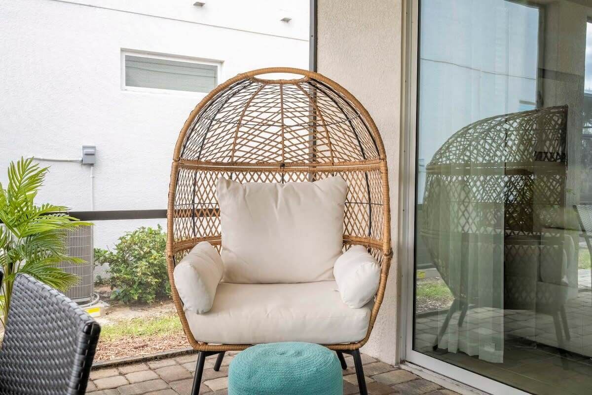 Une chaise en osier avec des coussins sur un balcon.