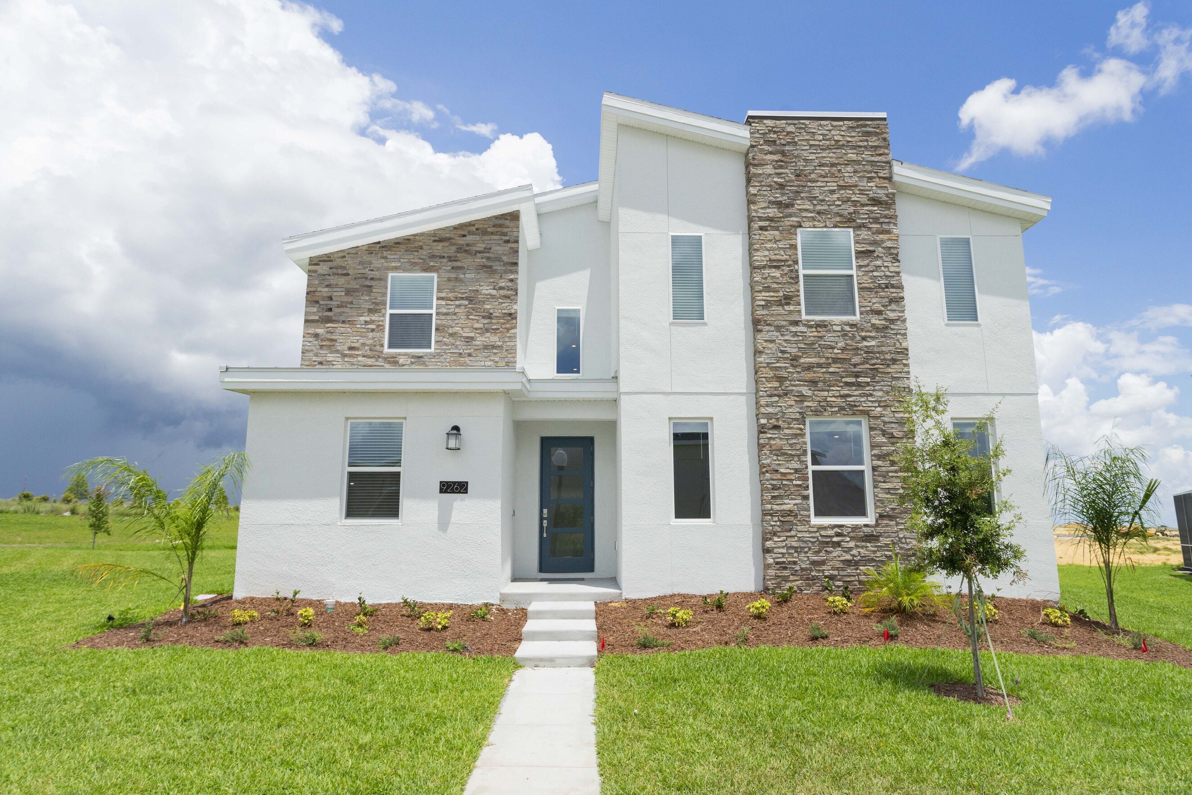 A modern two-story house with a stone facade, a front door, and a small front yard with young trees.