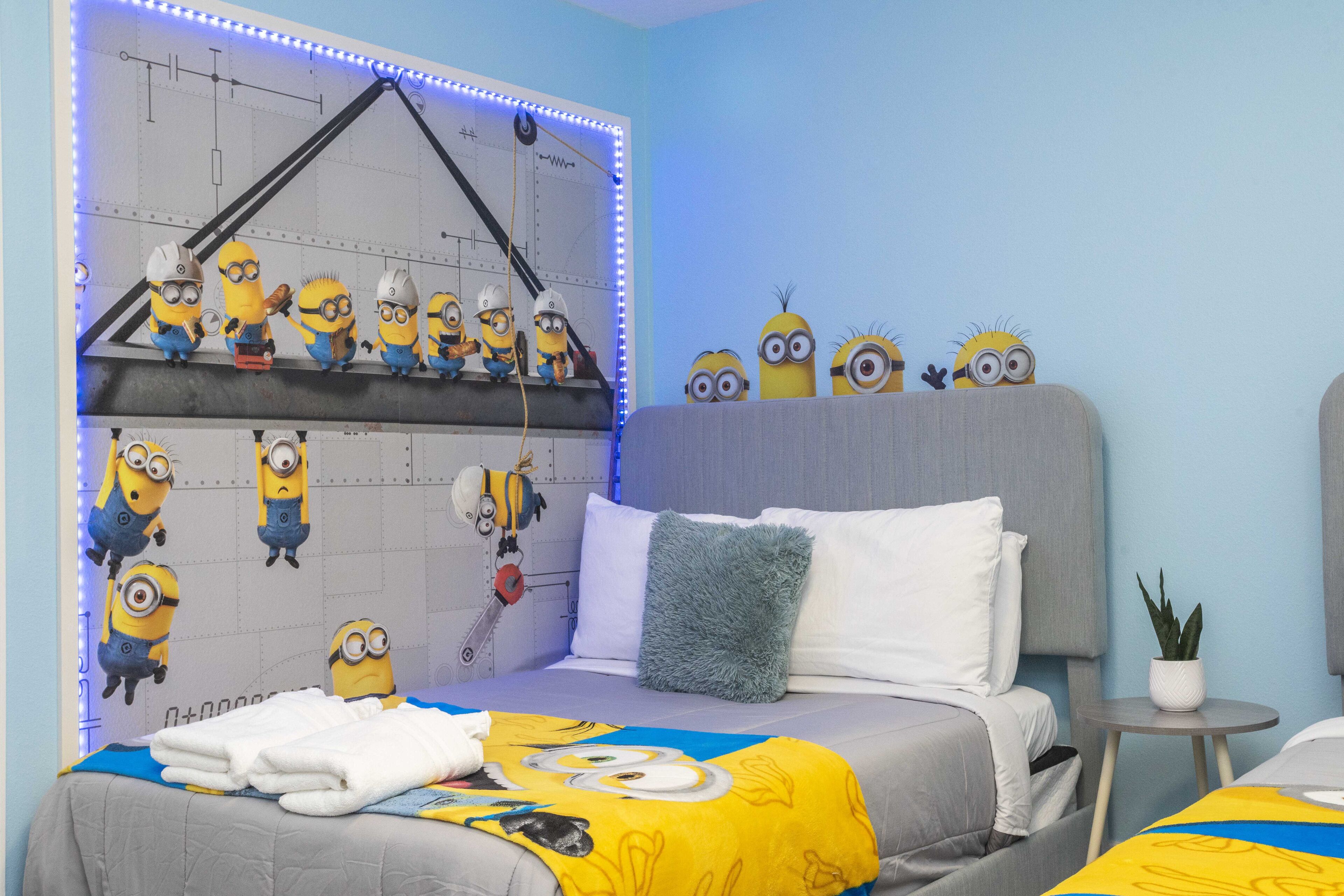 A bedroom with a bed, pillows, a nightstand, a wall with minion decorations, and a ceiling light fixture.