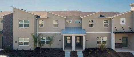 A modern multi-story residential building with a symmetrical facade, a central entrance with double doors, and a small front yard with landscaping.