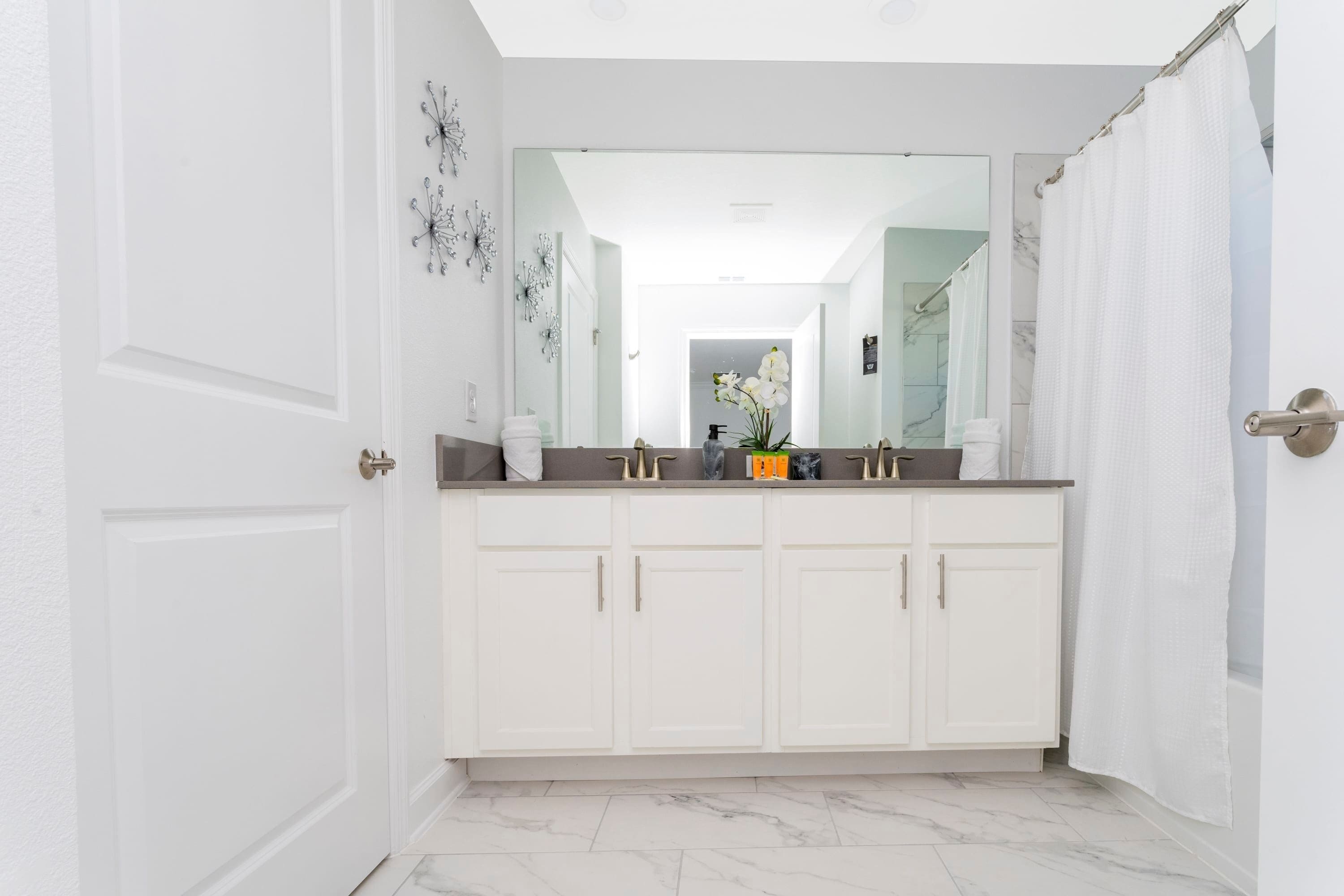 Een moderne badkamer met witte badkamerkasten, een grote spiegel en een marmeren vloer.