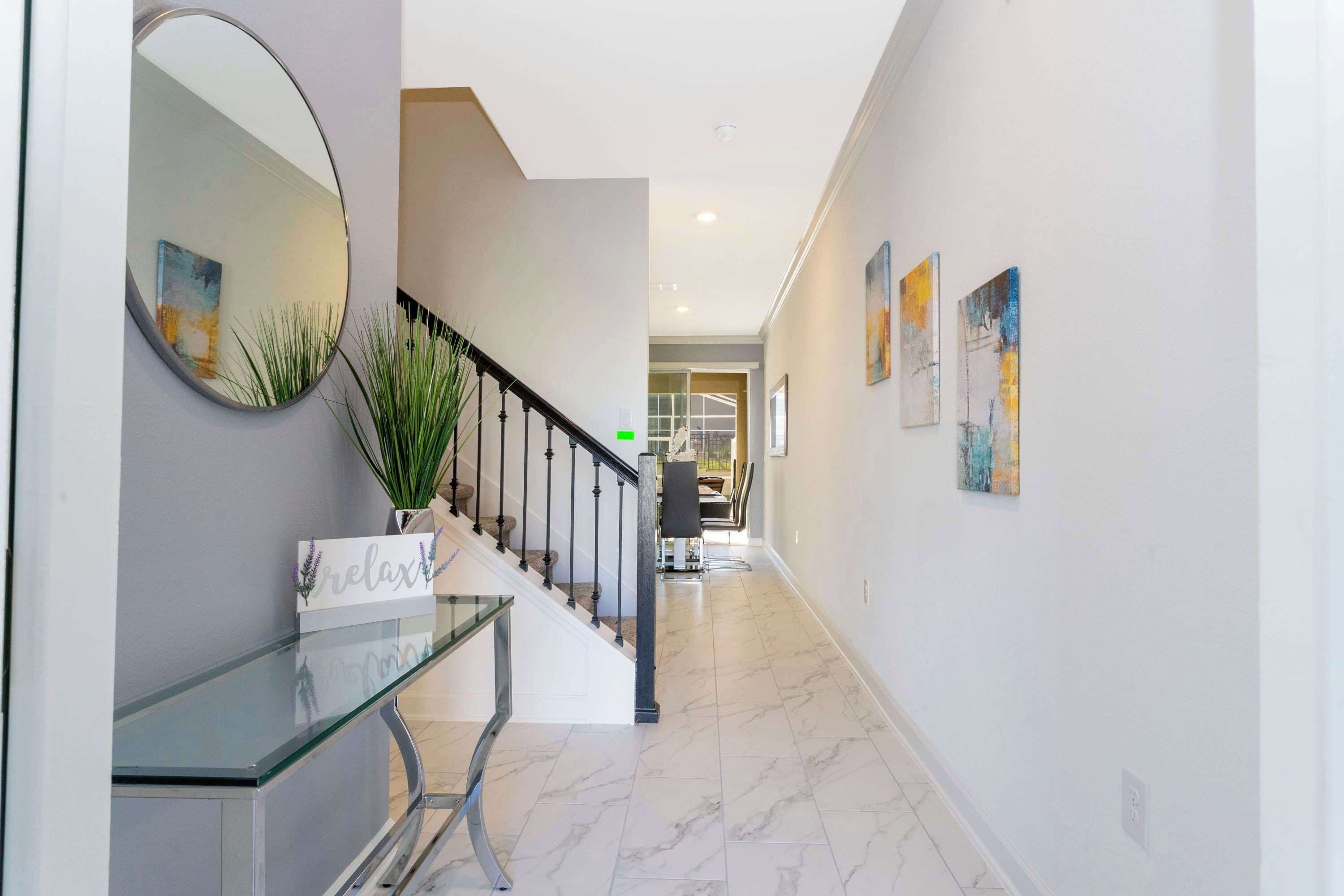 Un couloir moderne avec une console en verre, un miroir et un escalier.