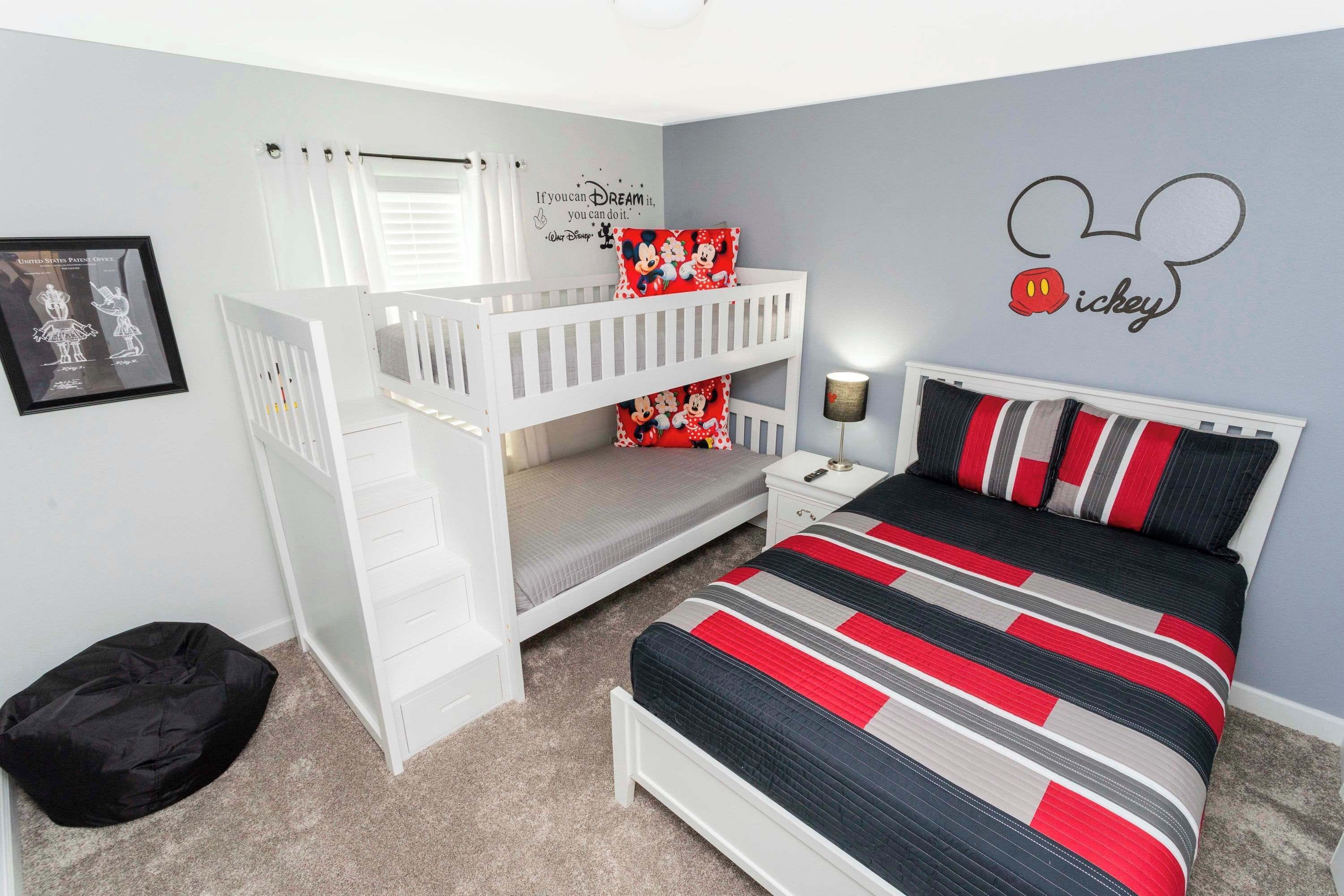 A bedroom with a bunk bed, a single bed with a striped bedspread, a Mickey Mouse wall decal, and a framed picture on the wall.