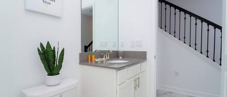 A bathroom with a toilet, sink, and mirror. There is a staircase with a black railing leading to another room.