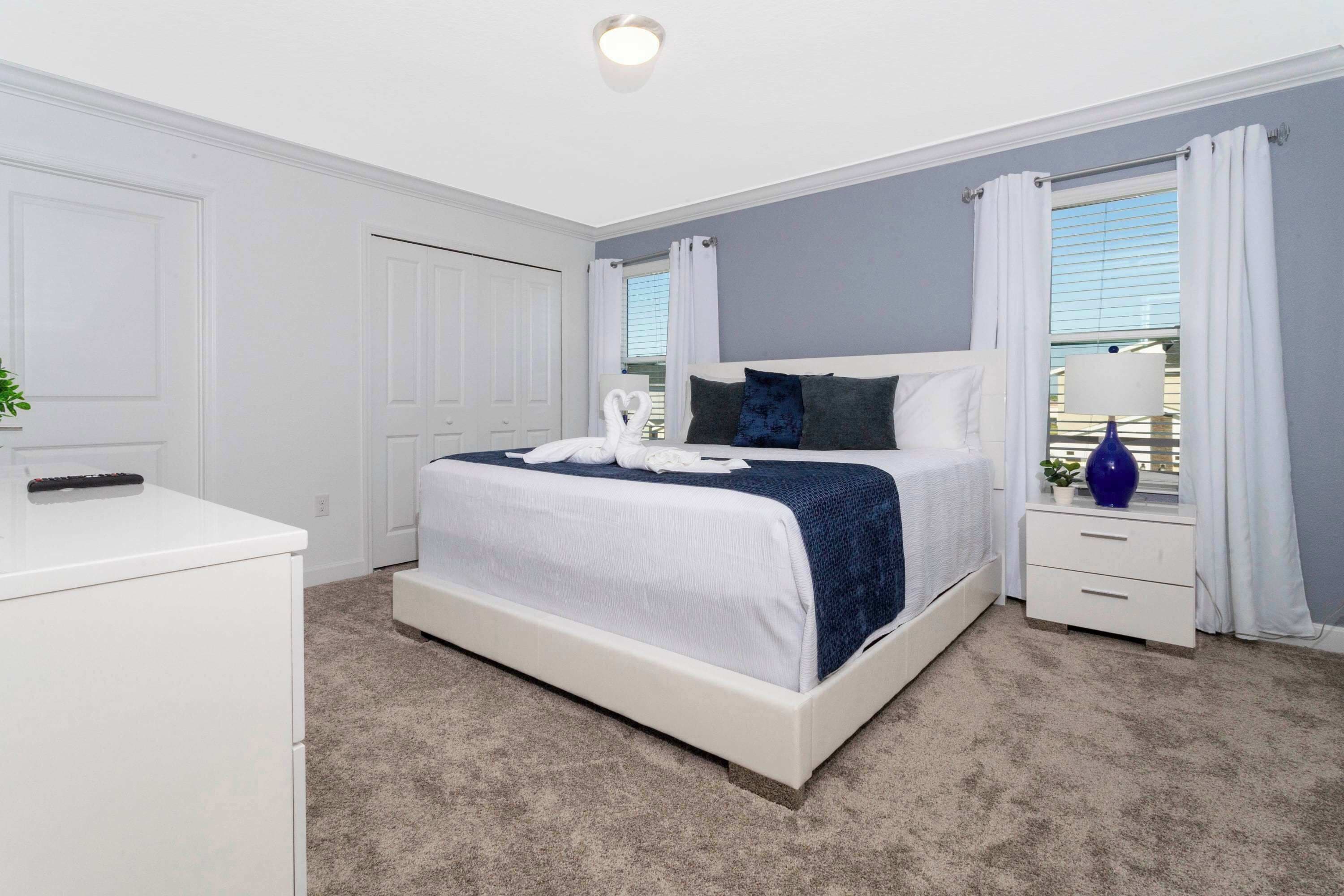 A bedroom with a bed, a nightstand, a dresser, and a window with curtains.