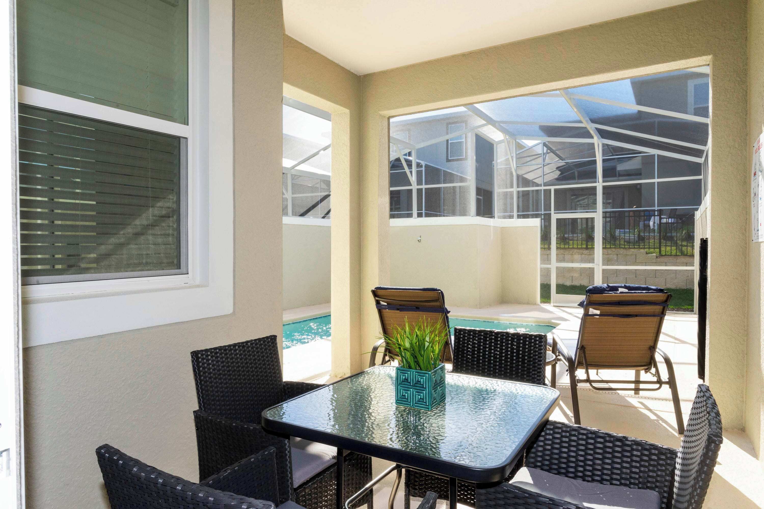 Ein Tisch mit Glasplatte, Korbstühle, ein Blumentopf und Blick auf Pool und Haus.