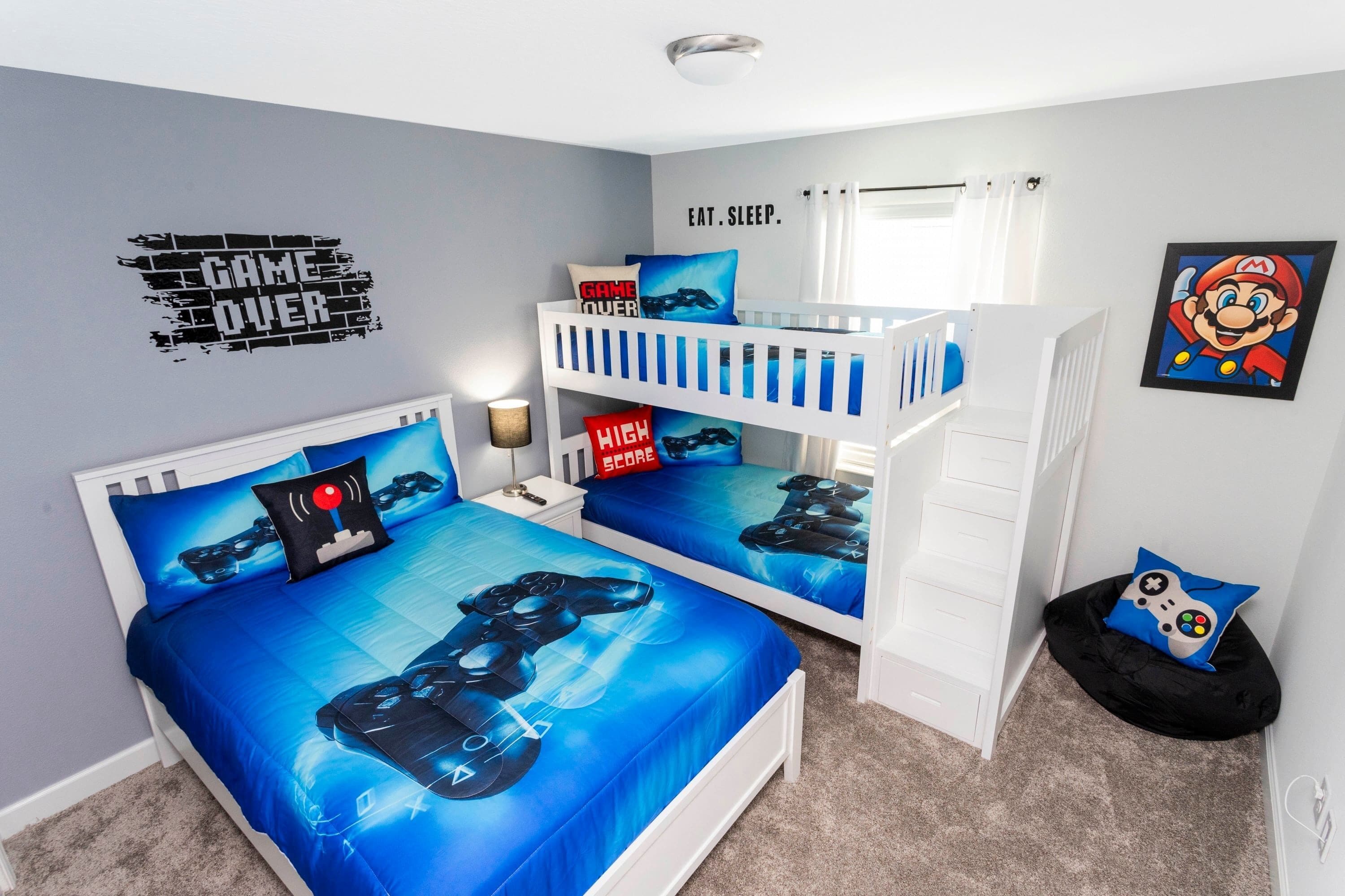 Ein Schlafzimmer mit Etagenbett, zwei Betten mit Gaming-Motiven, einer Wandsticker mit der Aufschrift „GAME OVER“, einem Gemälde zum Thema Mario und einem Kopfkissen mit „HIGH SCORE“.