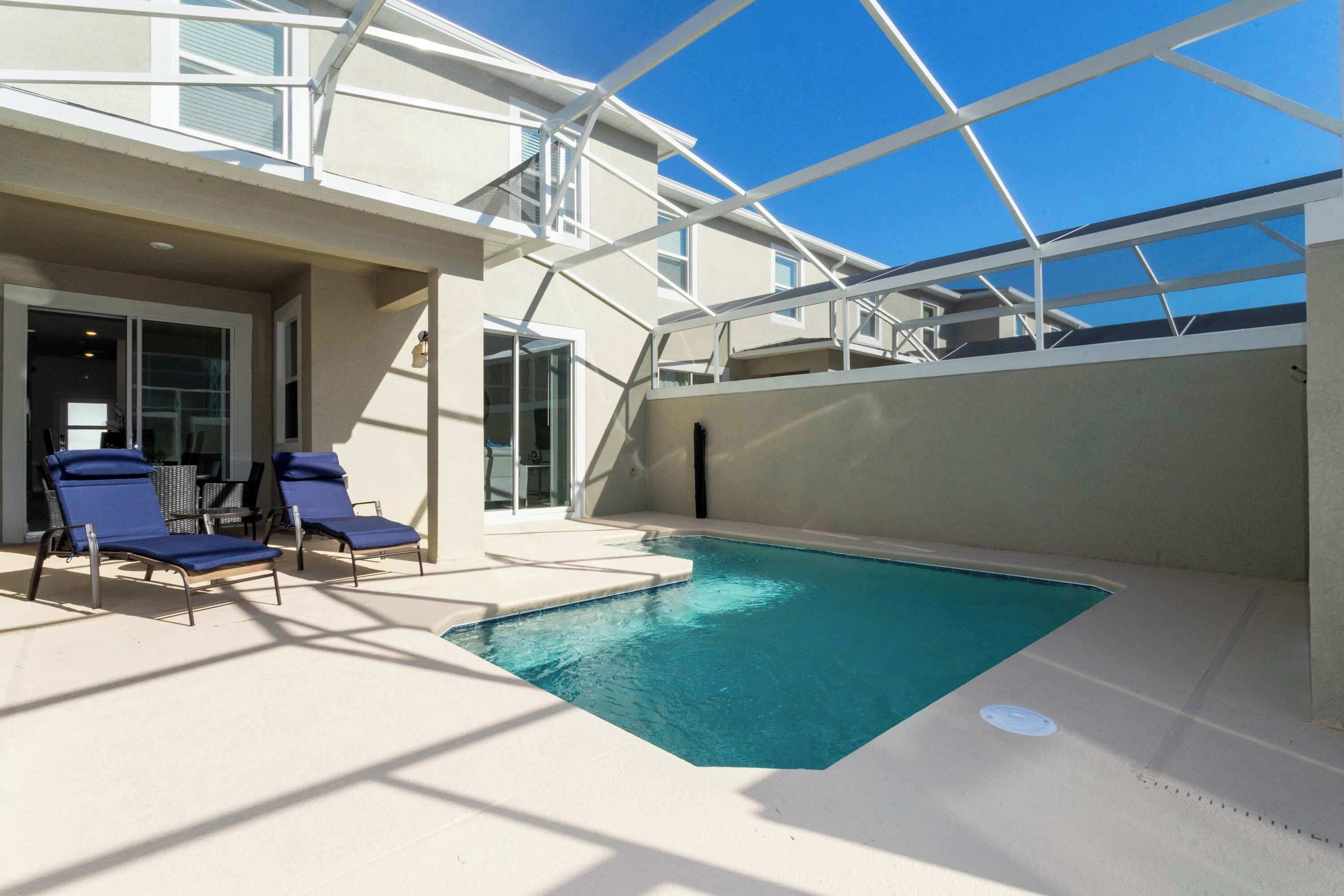 A pool area with two blue lounge chairs and a glass door leading to an interior space.