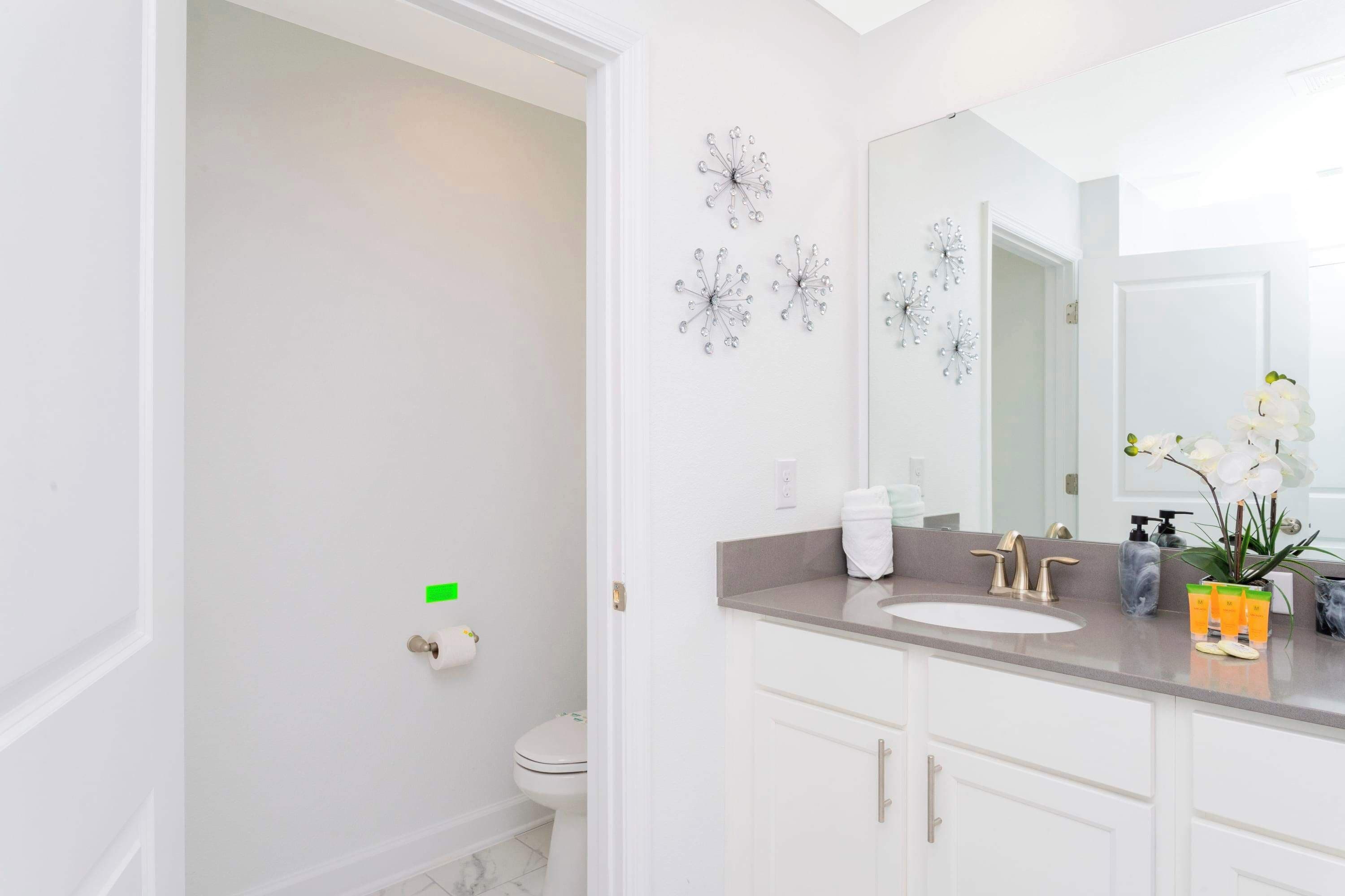 Une salle de bain moderne avec des toilettes blanches, un lavabo doté d’un grand miroir et des motifs décoratifs en forme de flocons de neige sur le mur.