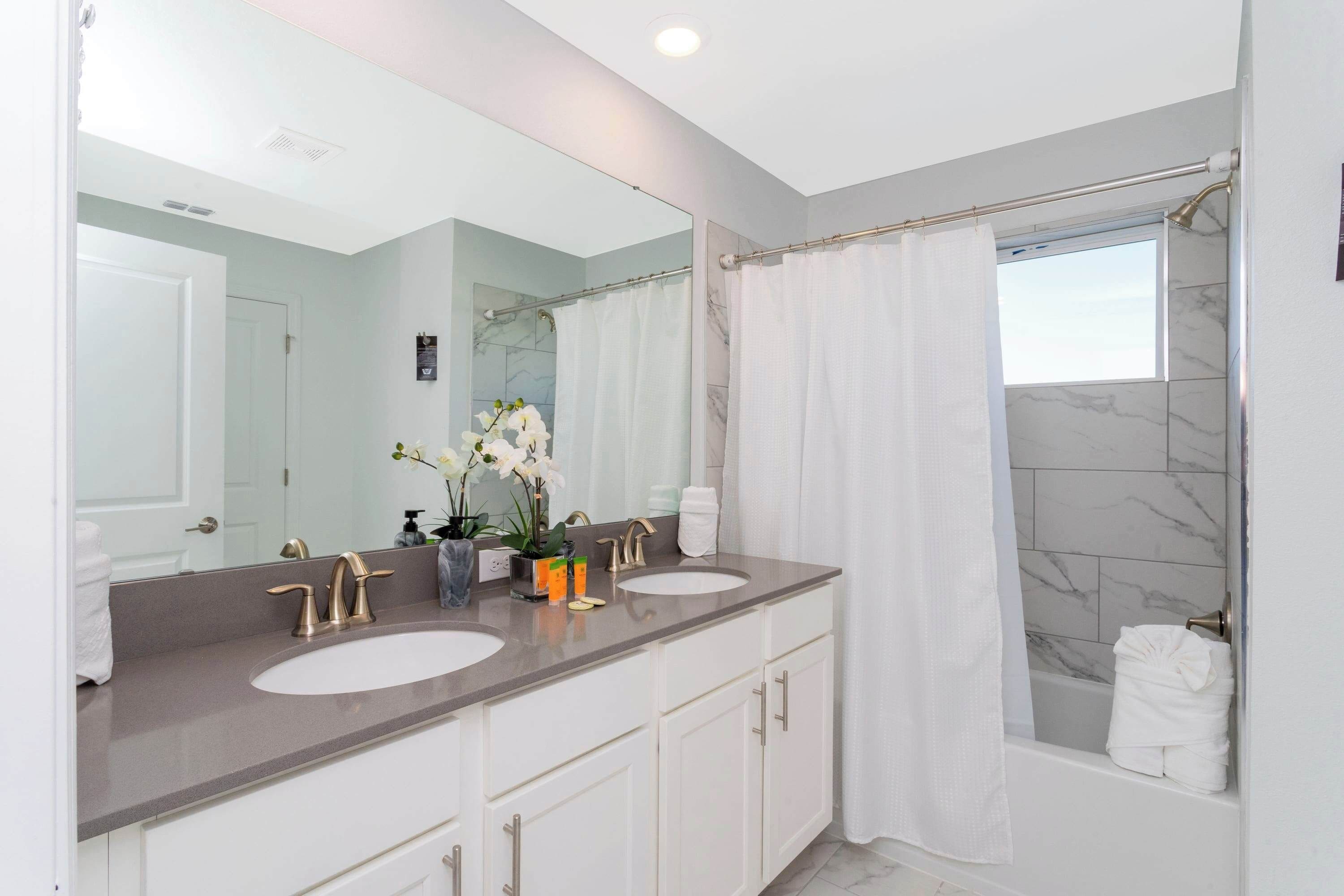 A modern bathroom with two sinks, a large mirror, and a shower area.