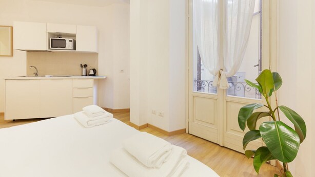 A hotel room with a bed, a small kitchenette, a balcony with curtains, and a potted plant. - GuestHost - Studio Milan-Corso Magenta! Ac & Wifi! (Milano)