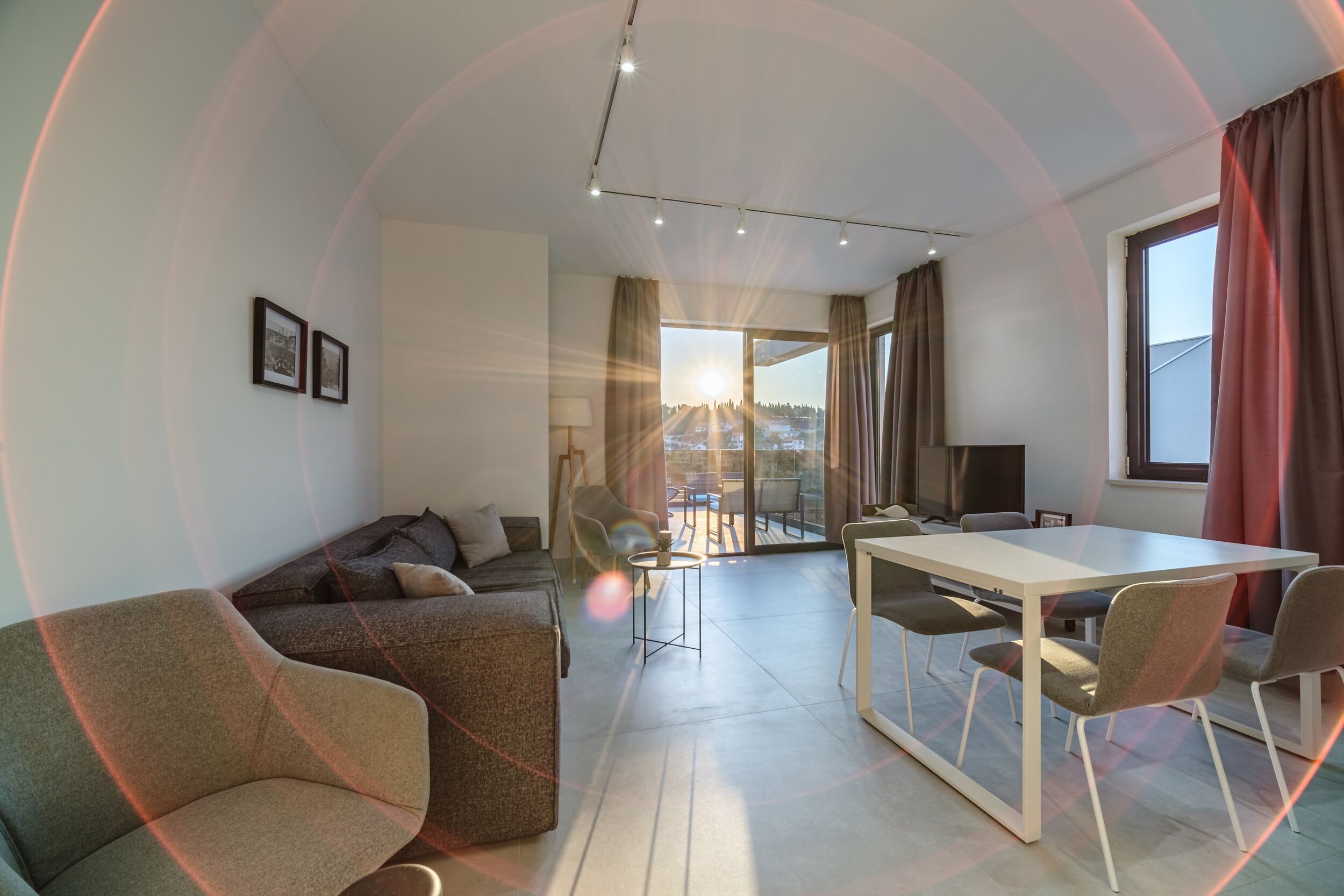 A modern living room with a sofa, a dining table with chairs, a TV, and a balcony with a view.