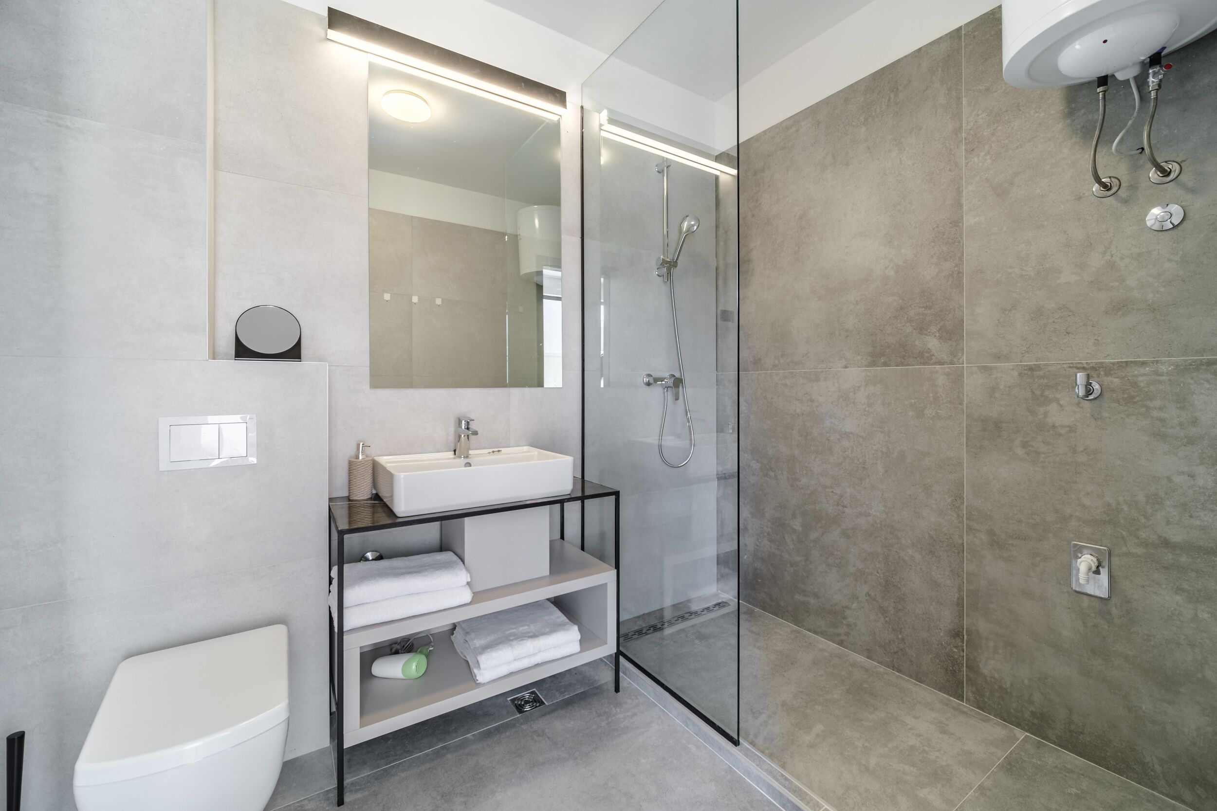 A modern bathroom with a glass-enclosed shower, a white sink, and a built-in shelf with towels.