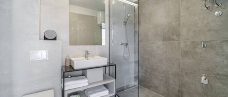 A modern bathroom with a glass-enclosed shower, a white sink, and a built-in shelf with towels.