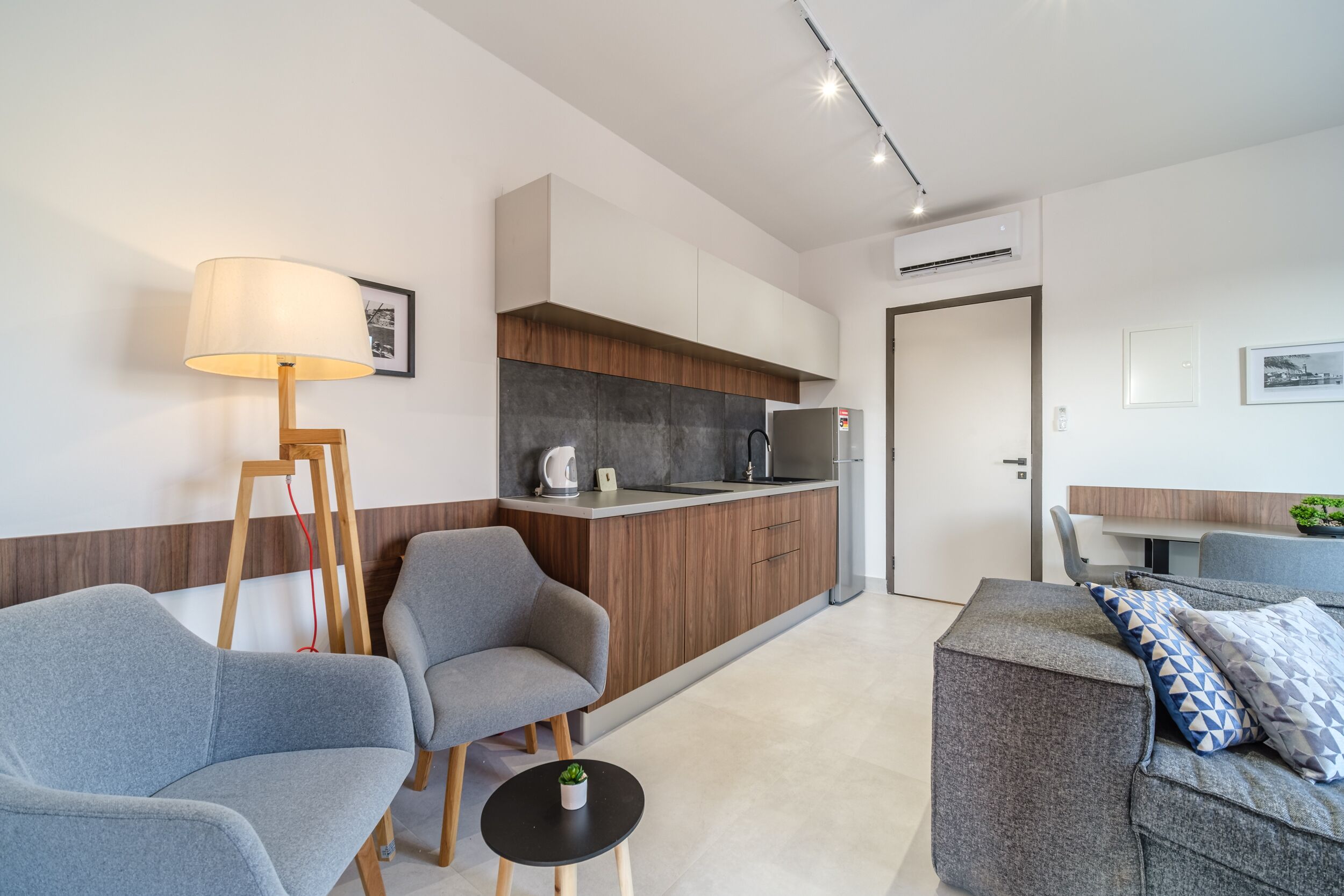 Una sala de estar moderna con sofás grises, una mesita negra y una lámpara de pie de madera.