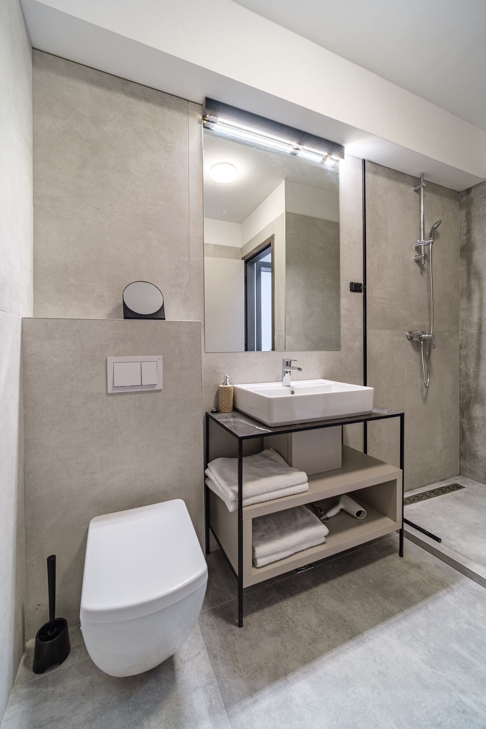 Un baño moderno con inodoro blanco, un lavamanos con espejo y zona de ducha.