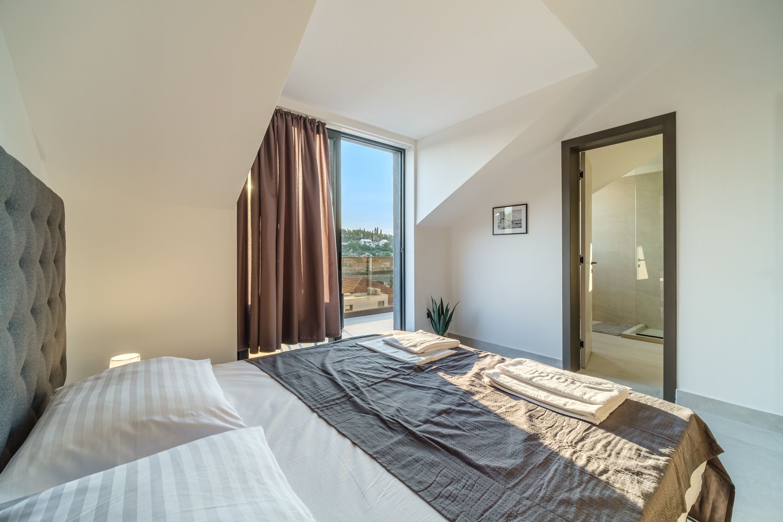 A bedroom with a large bed, a view of the outdoors, and a sliding door to a bathroom.