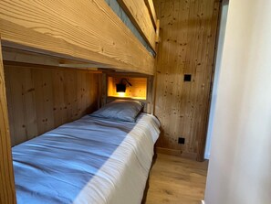 A single bed in a wooden room with a sloped ceiling and a small window.