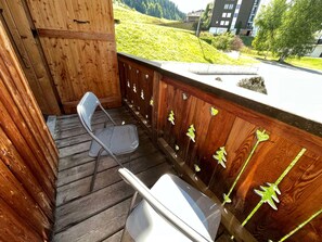 A wooden deck with a metal chair and a white table. - Renovated and comfortable apartment, perfect for family of 4 (Les Gets)