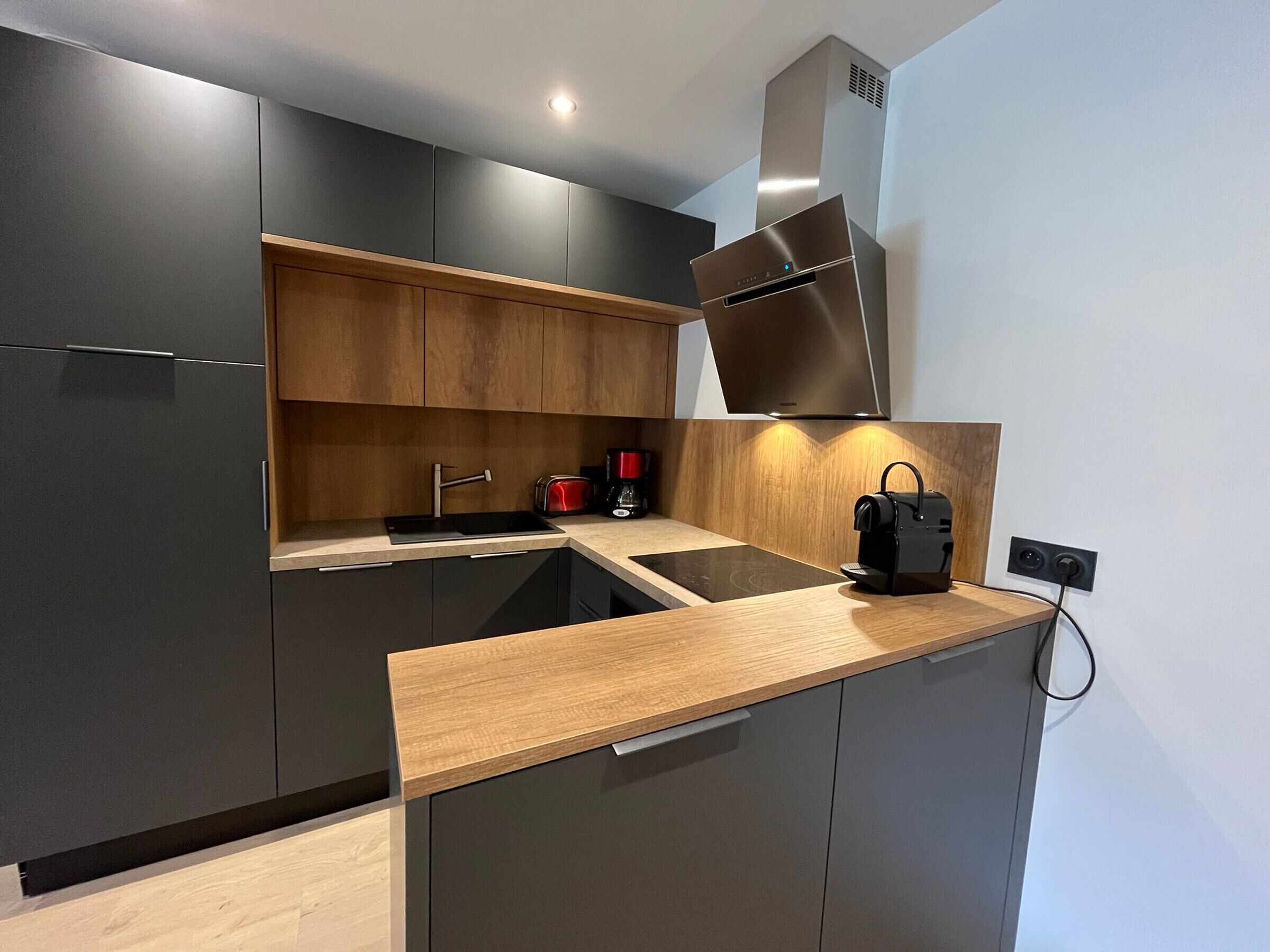 Una cocina moderna con armarios oscuros, encimera de madera, extractor de acero inoxidable y una cafetera.
