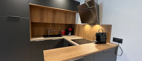 Una cocina moderna con armarios oscuros, encimera de madera, extractor de acero inoxidable y una cafetera.